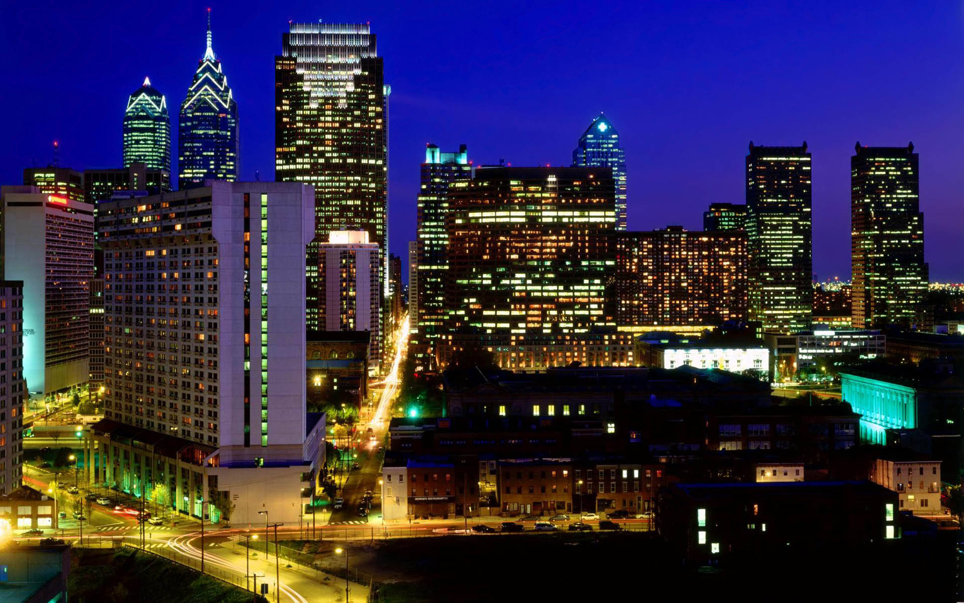 Philadelphia 桌布 壁紙 — 深藍色天空下，閃爍的摩天大樓與發光的街道構成的充滿活力的夜景城市天際線。