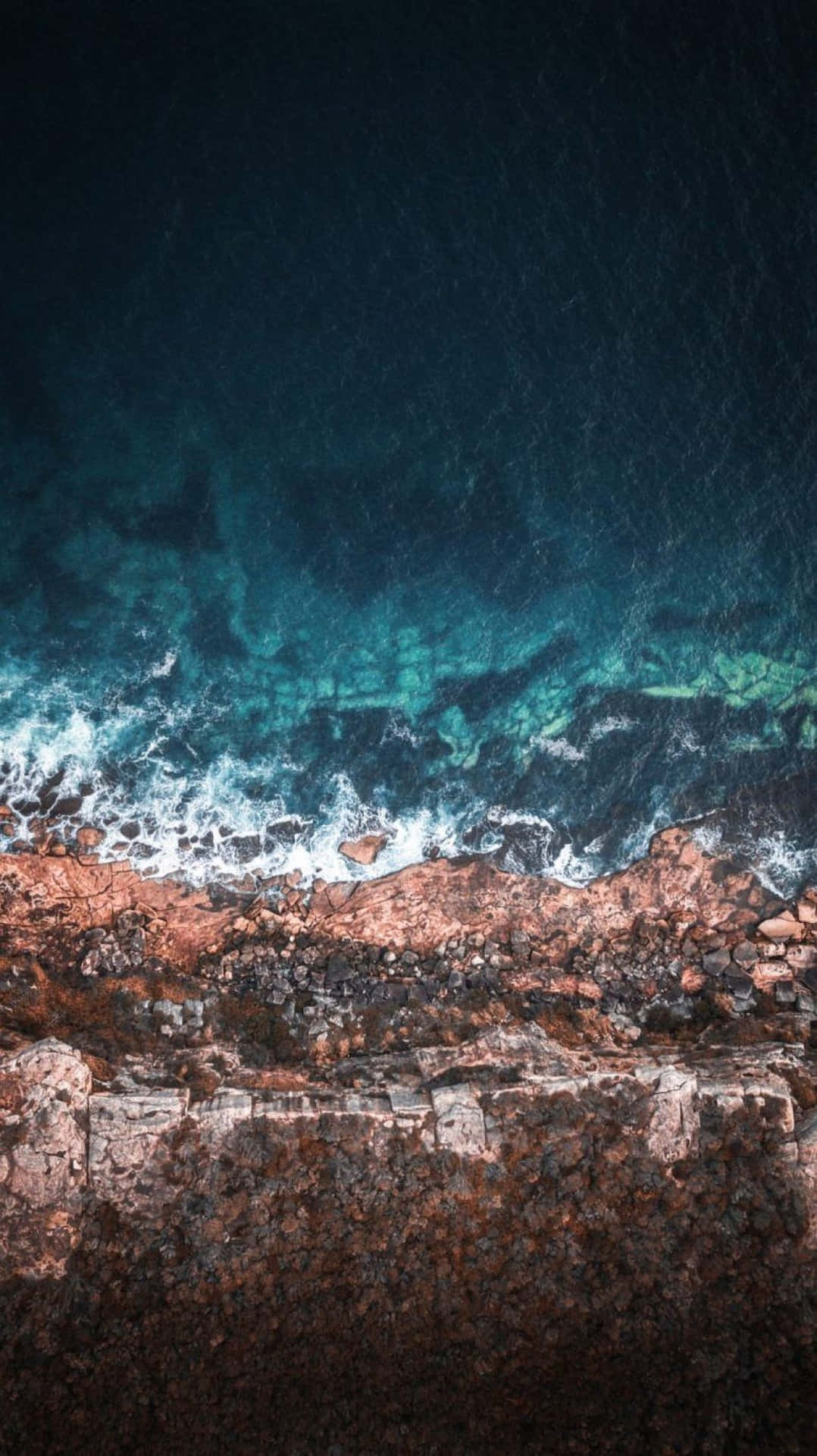 Cyan 桌布 壁紙 — 深藍色海洋下，綠松石色的海浪拍打著崎嶇的棕色懸崖的鳥瞰圖。