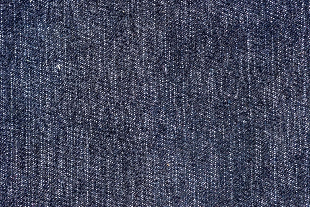 Denim Blue 桌布 壁紙 — 深藍色牛仔布料的特寫，顯示出有紋理的編織和垂直線條圖案的微妙褪色。