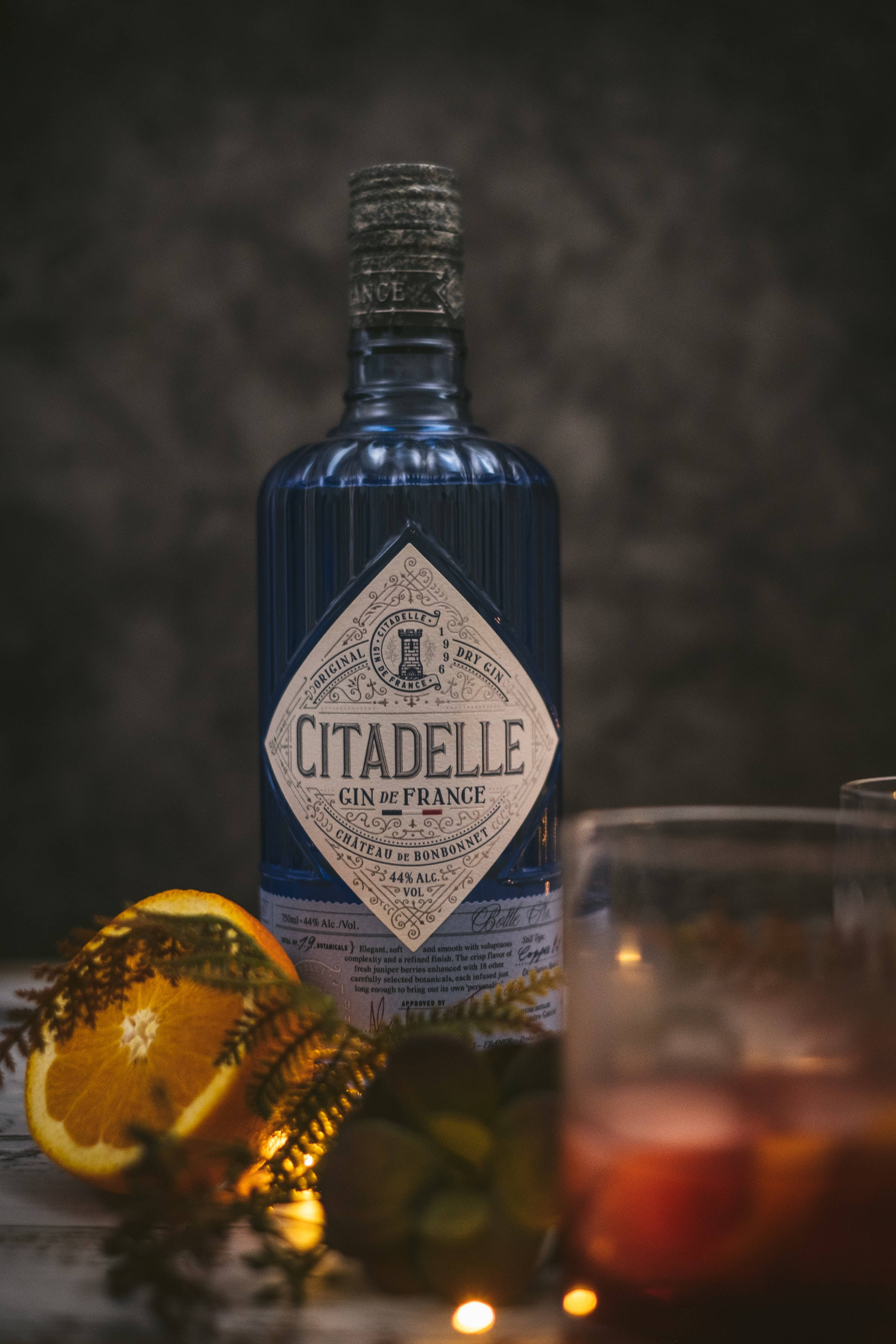 drinks 桌布 壁紙 — 深藍色的Citadelle琴酒瓶站在一個發光的雞尾酒和柳橙片旁邊，背景是深色有紋理的。