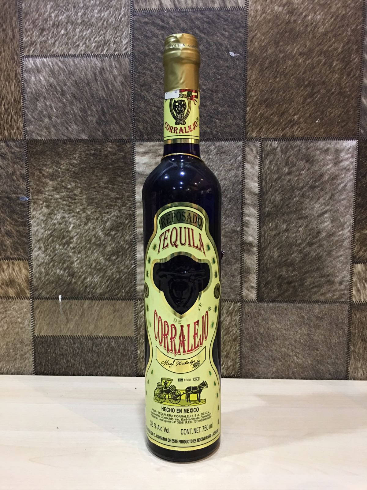 bottle 桌布 壁紙 — 深藍色的Corralejo Reposado龍舌蘭酒瓶置於淺色木質表面中央，背景為棕色牛皮瓷磚牆。