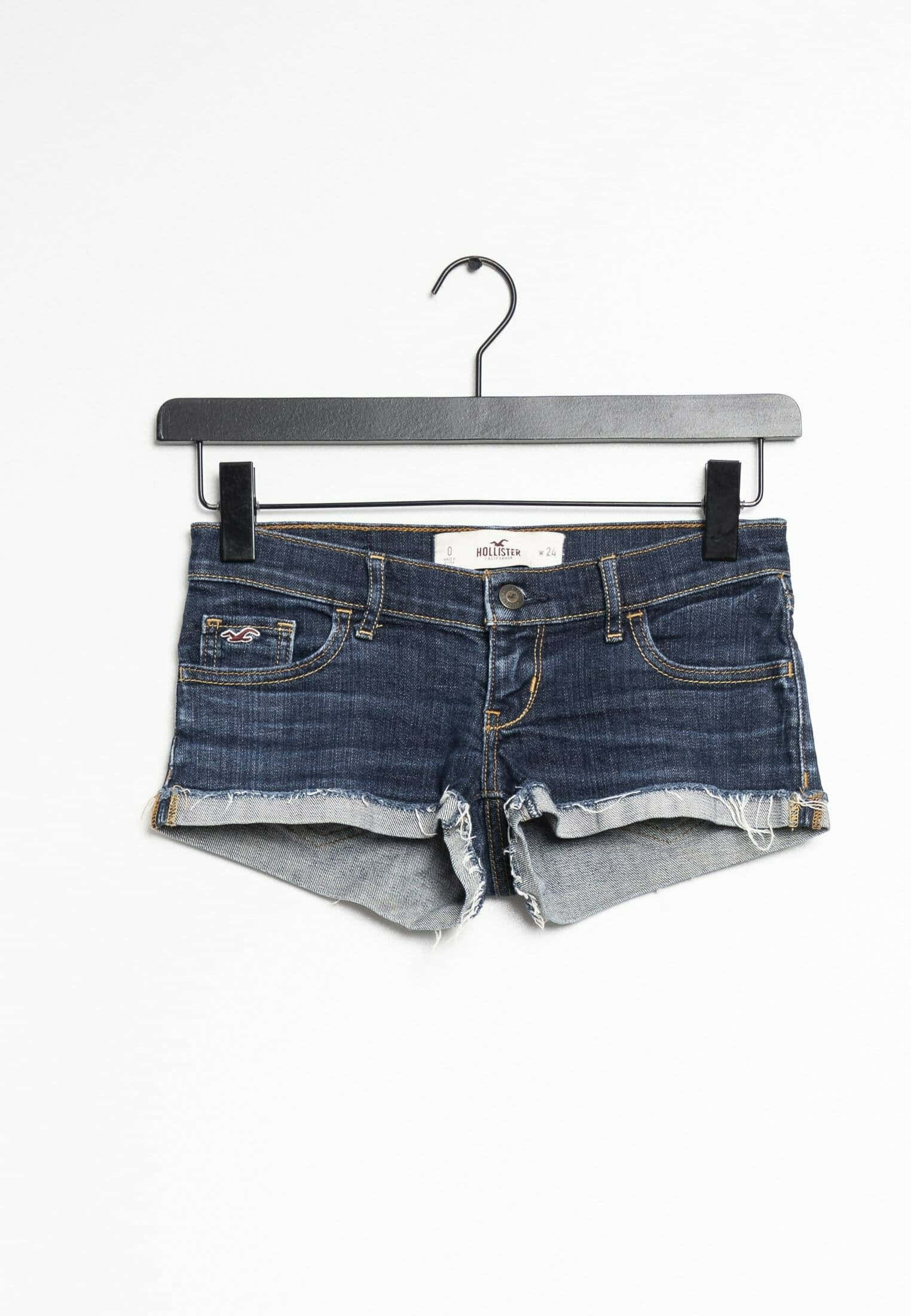 Hollister 桌布 壁紙 — 深藍色磨邊牛仔短褲整齊地掛在黑色衣架上，背景為純白色。