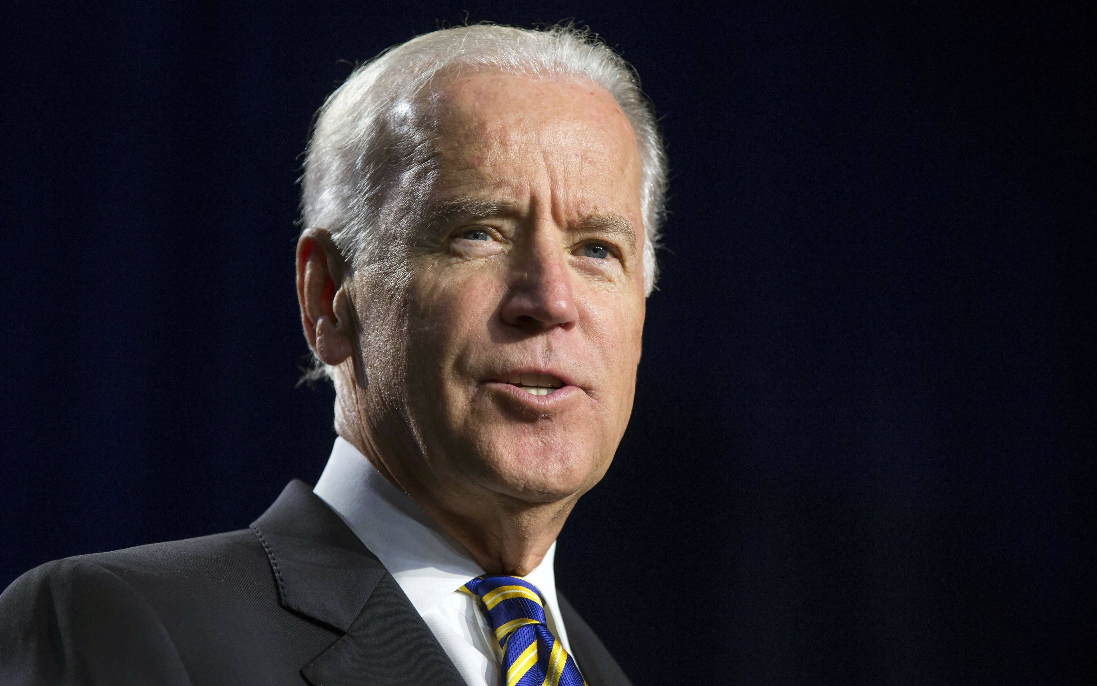 Biden 桌布 壁紙 — 深藍色背景下，身穿深色西裝、繫著藍黃條紋領帶的男士特寫肖像。