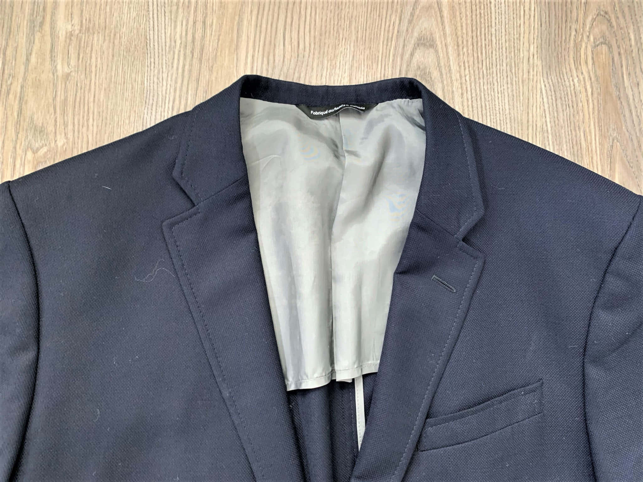 Mens Fashion 桌布 壁紙 — 深藍色西裝外套平放在淺色木質表面上，展示其領口和緞面襯裡的近距離特寫。
