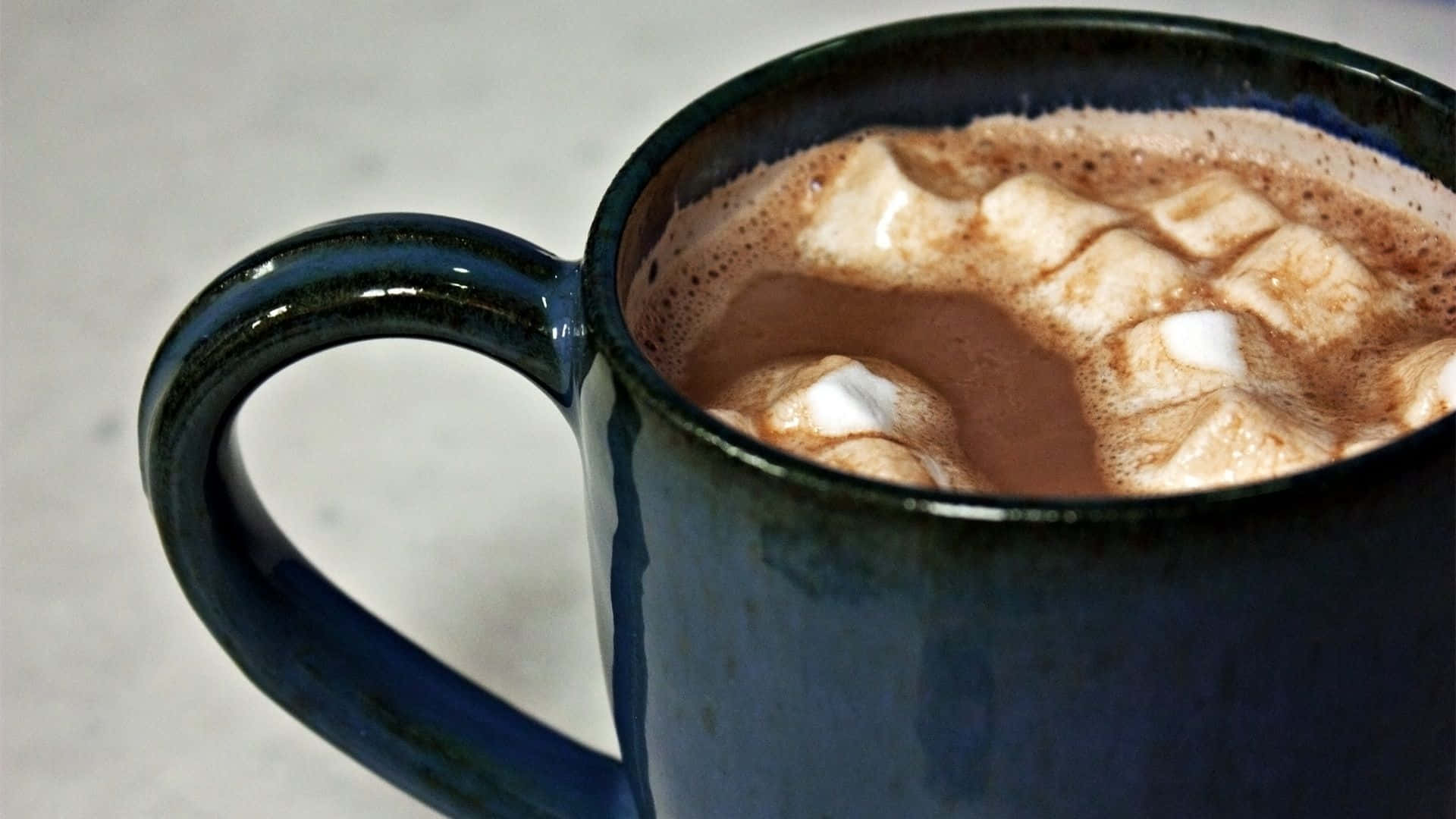 Hot Chocolate 桌布 壁紙 — 深藍色陶瓷杯的特寫，裝滿冒著熱氣的熱巧克力，上面放著蓬鬆的白色棉花糖。