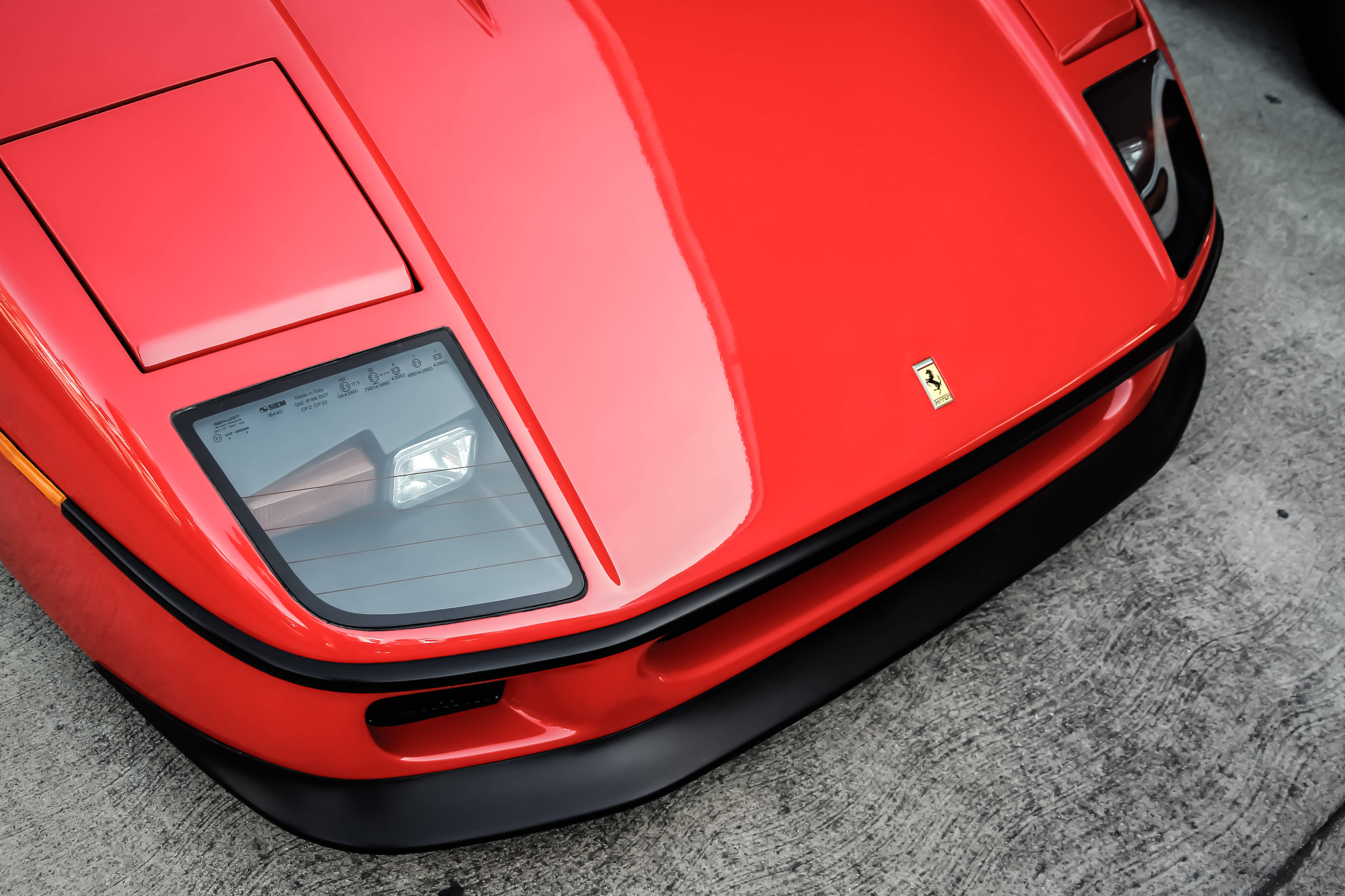 ferrari f1 2018 桌布 壁紙 — 混凝土上紅色法拉利跑車引擎蓋的特寫，帶有標誌性的躍馬標誌。