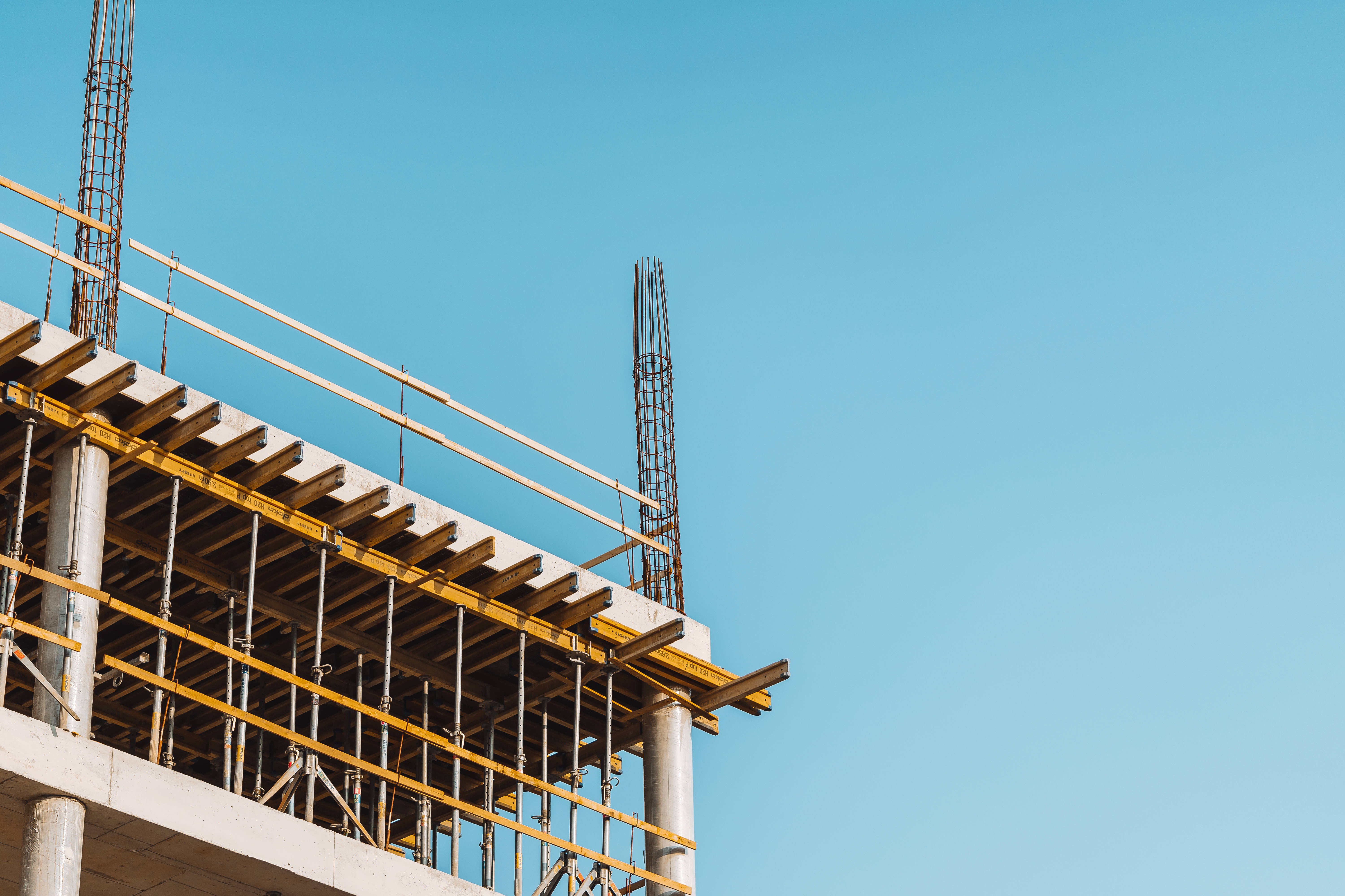 Building 桌布 壁紙 — 混凝土建築物施工中的近距離特寫，帶有黃色鷹架，背景是晴朗的藍天。