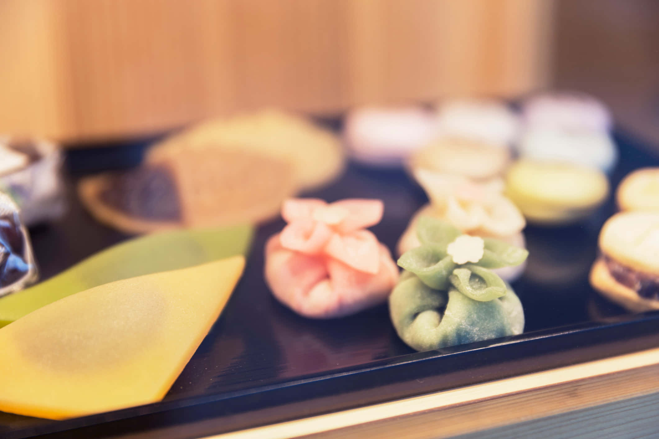 Japanese Sweets 桌布 壁紙 — 淺景深凸顯了深色托盤上色彩繽紛的日本麻糬糰子，背景甜點模糊。