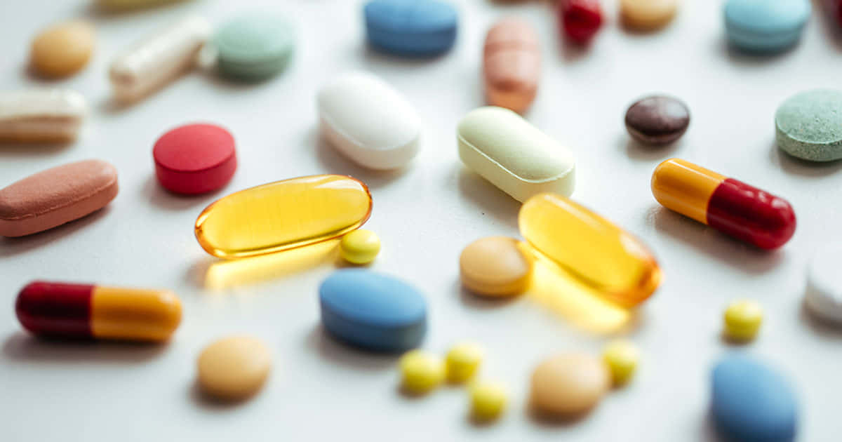 pills 桌布 壁紙 — 淺景深特寫，各種彩色藥丸和膠囊散落在明亮的白色表面上。