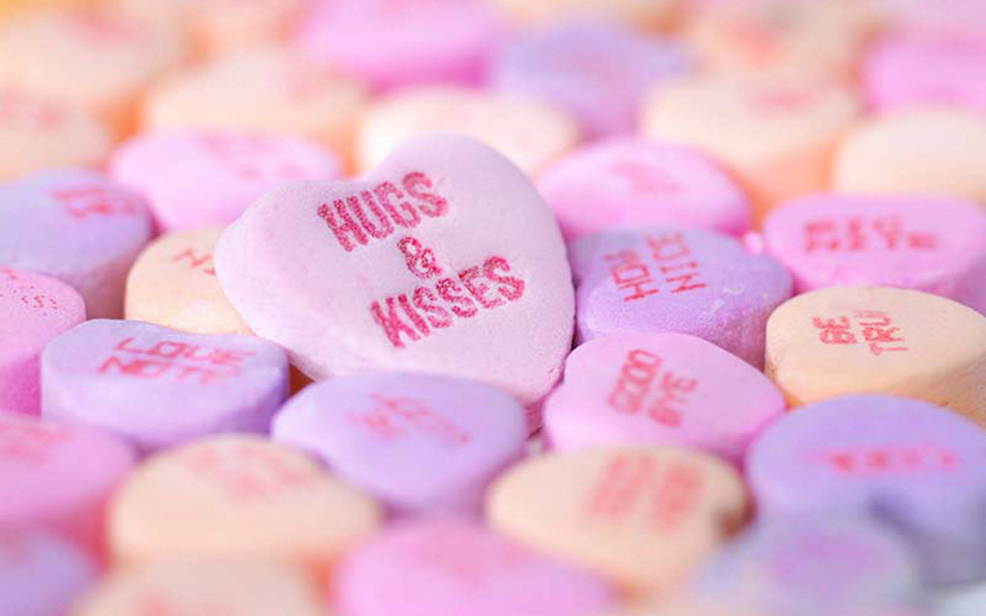 糖果 桌布 壁紙 — 淺景深特寫，柔焦中散落著帶有紅色訊息（如 hugs kisses）的粉彩心形糖果。