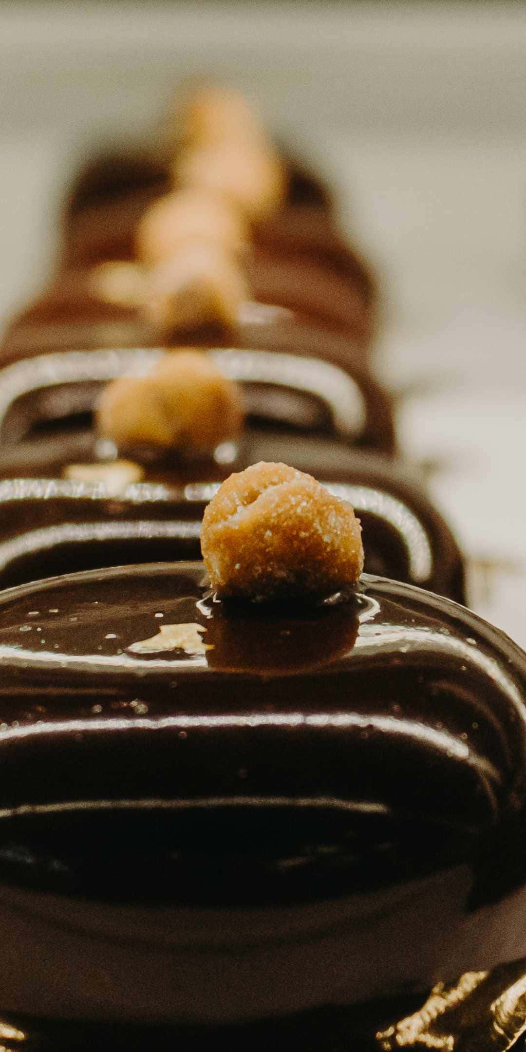 Chocolate 桌布 壁紙 — 淺景深特寫，閃亮的巧克力外皮糕點排列整齊，上面有焦糖糖衣。