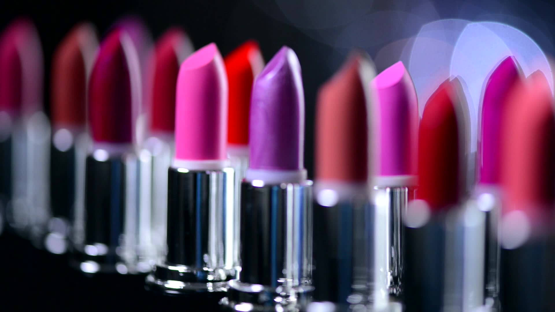 Cosmetics 桌布 壁紙 — 淺景深突出了在帶有散景燈光的深色背景上的鮮豔粉紅色和紫色唇膏。