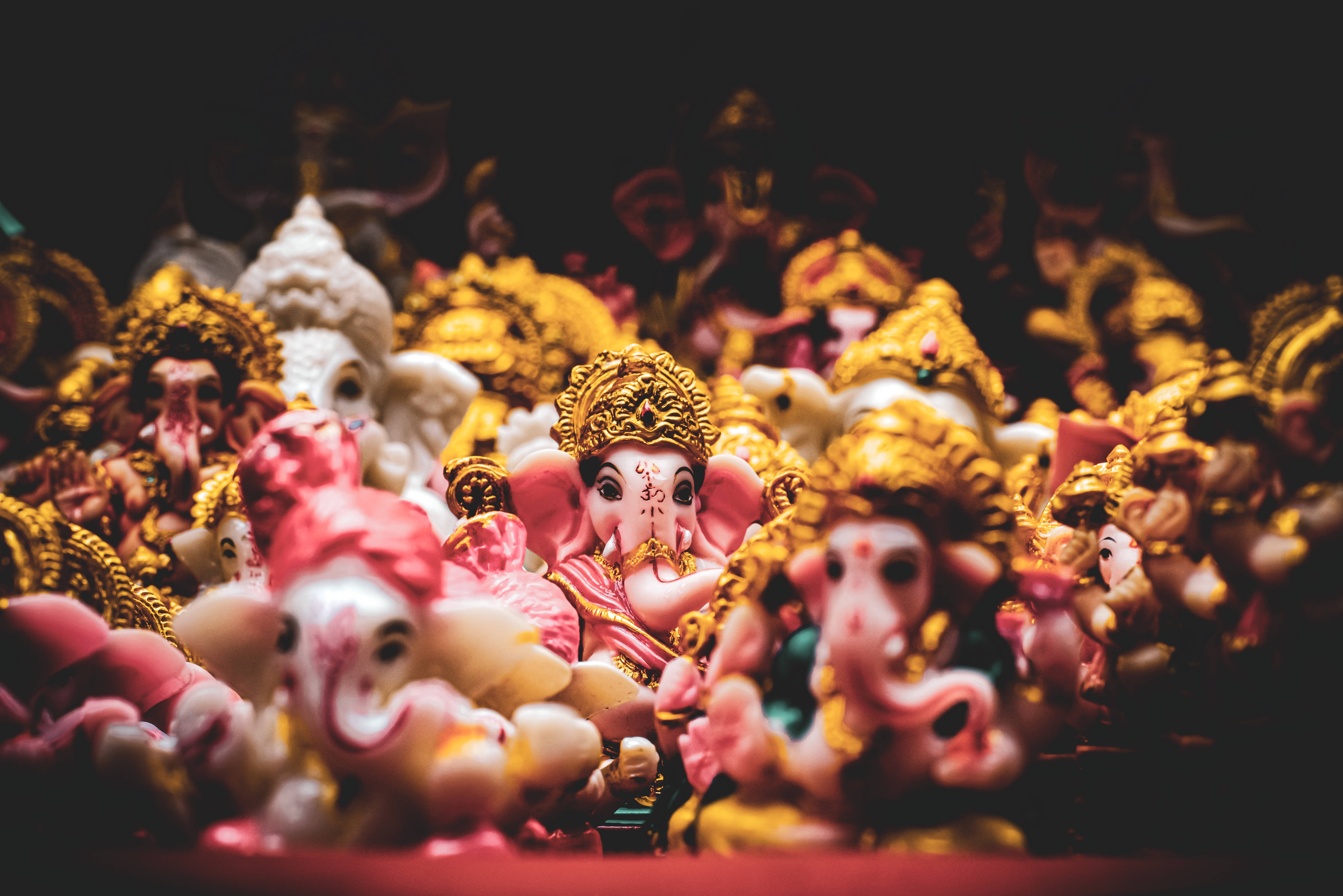 Bappa 桌布 壁紙 — 淺景深突出了金色和色彩繽紛的印度教神像海洋中的中央粉紅色象頭神雕像。