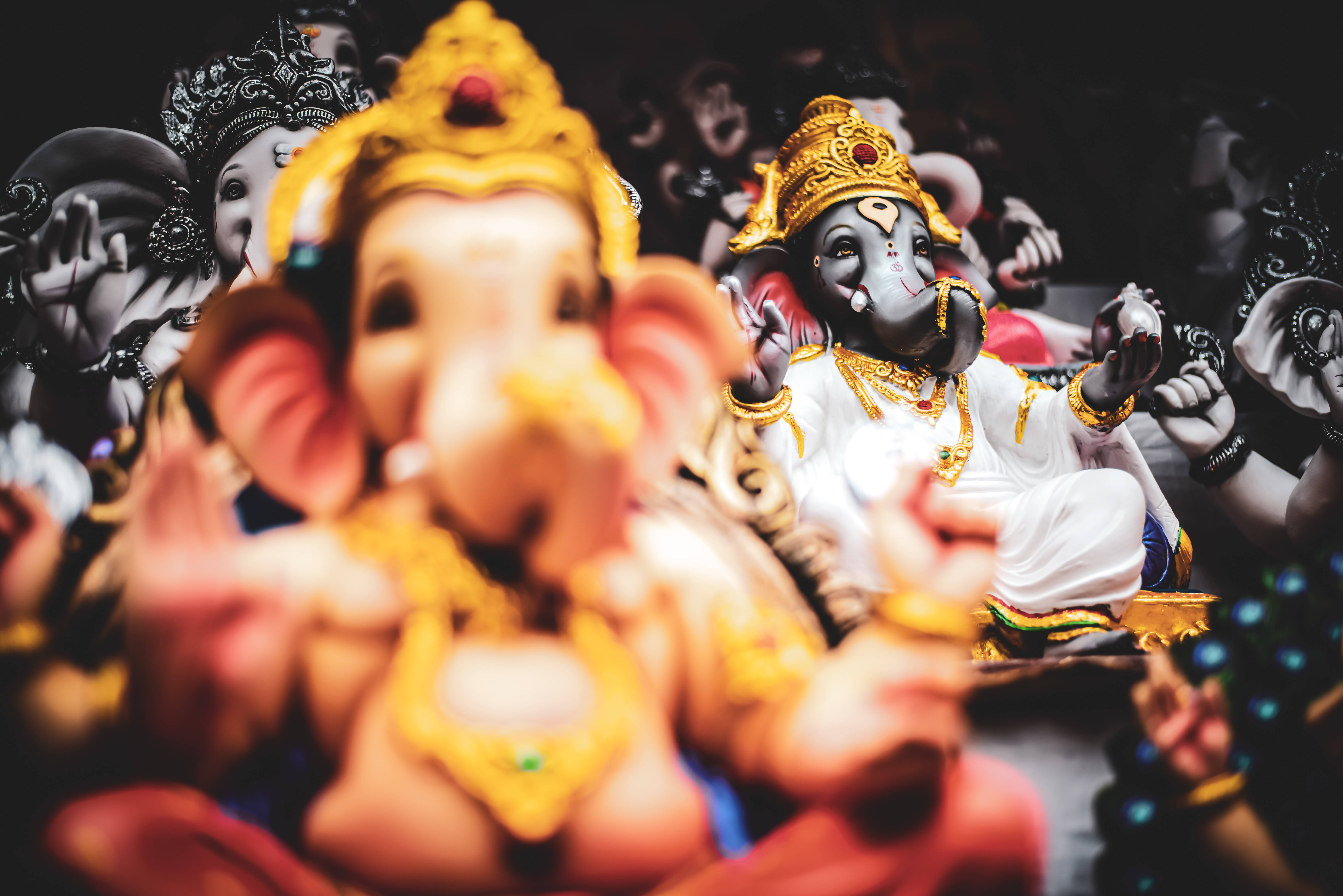 Bappa 桌布 壁紙 — 淺景深突出前景的金色象神雕像，其他雕像在黑暗環境中模糊在後。