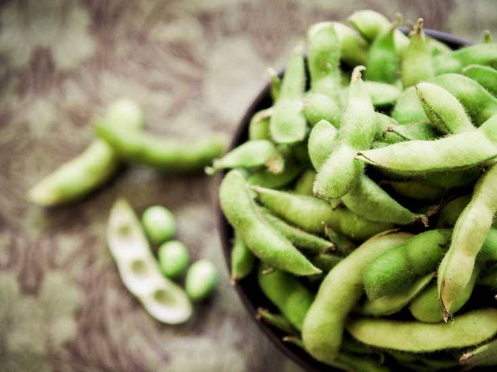 Vegetables 桌布 壁紙 — 淺景深突顯了深色碗中的新鮮綠色毛豆莢，豆子散落在有紋理的表面上。