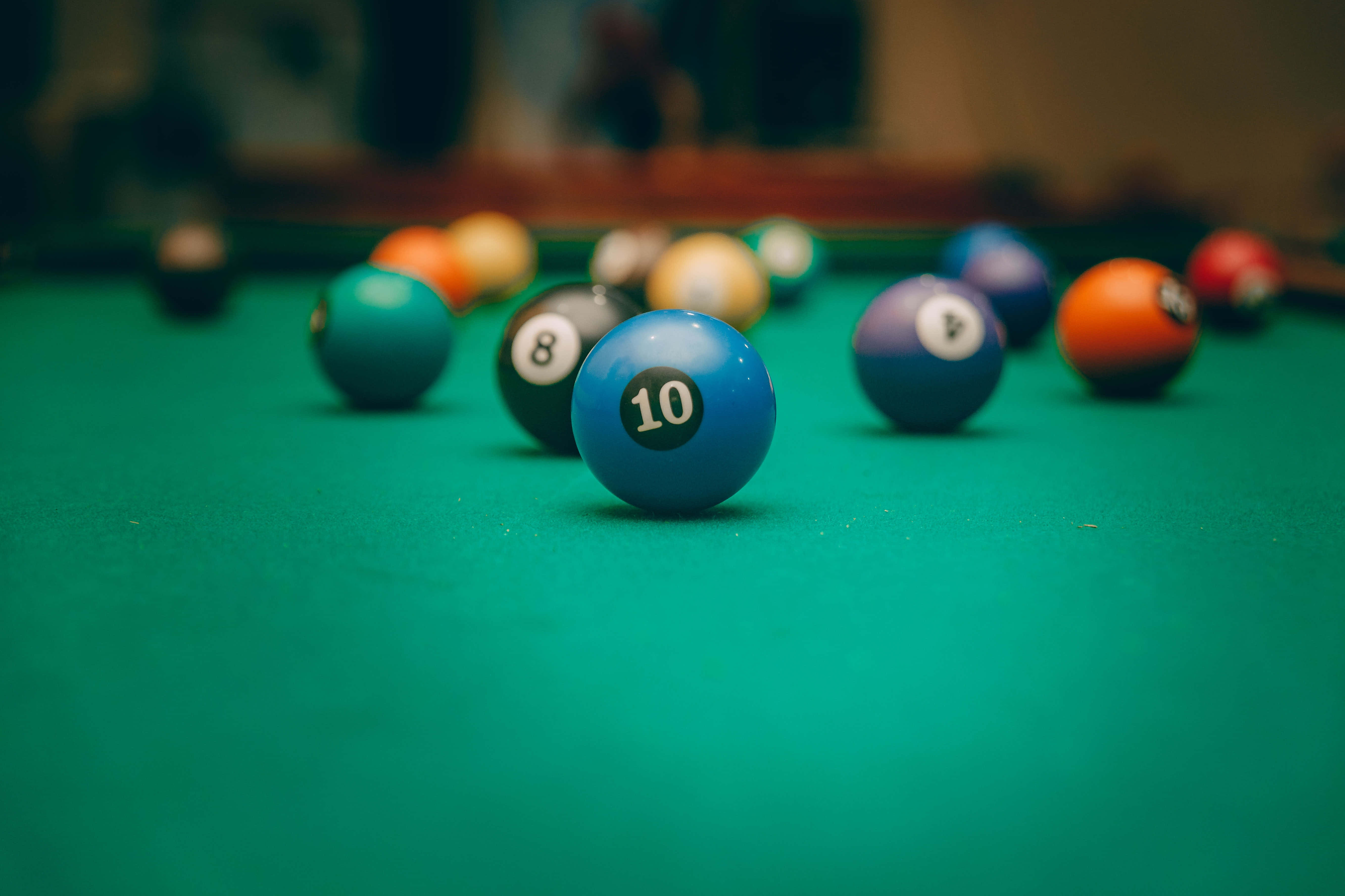 balls 桌布 壁紙 — 淺景深聚焦於一顆藍色撞球十號球，它靜置在鮮綠色絨布桌面上，背景中的其他球體模糊不清。