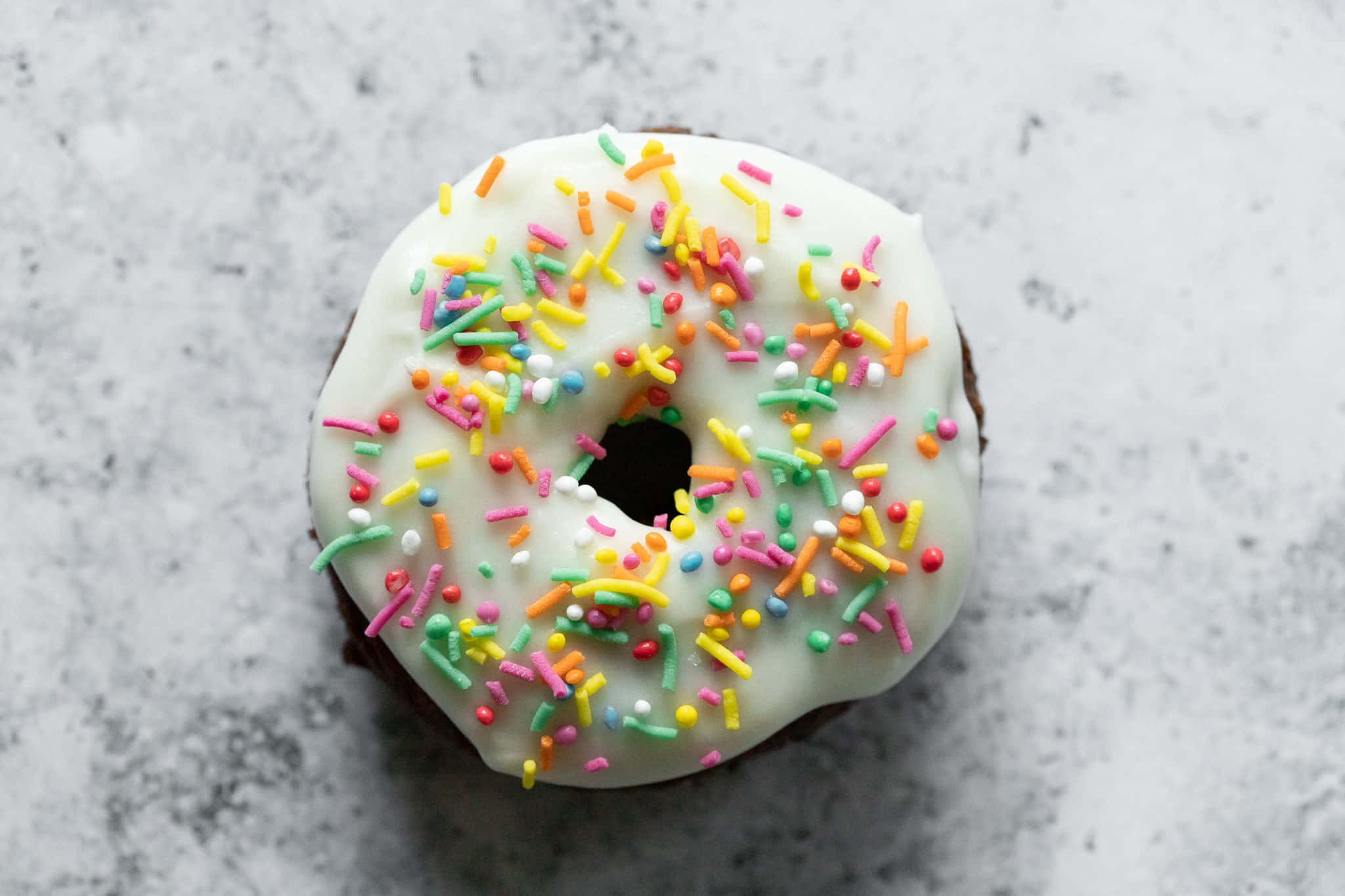 Donut 桌布 壁紙 — 淺灰色大理石表面上，一個帶有白色糖霜和彩色糖粒的巧克力甜甜圈的俯視圖。
