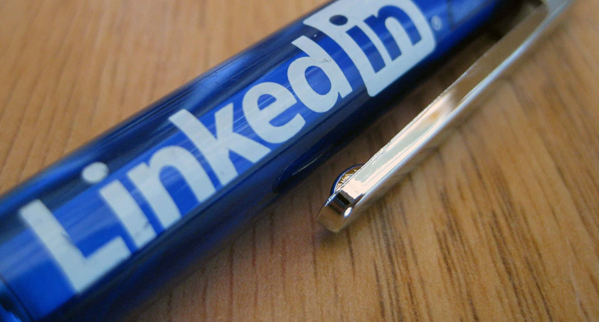 Linkedin Logo 桌布 壁紙 — 淺色木紋表面上斜放著一支藍色LinkedIn品牌筆的特寫。
