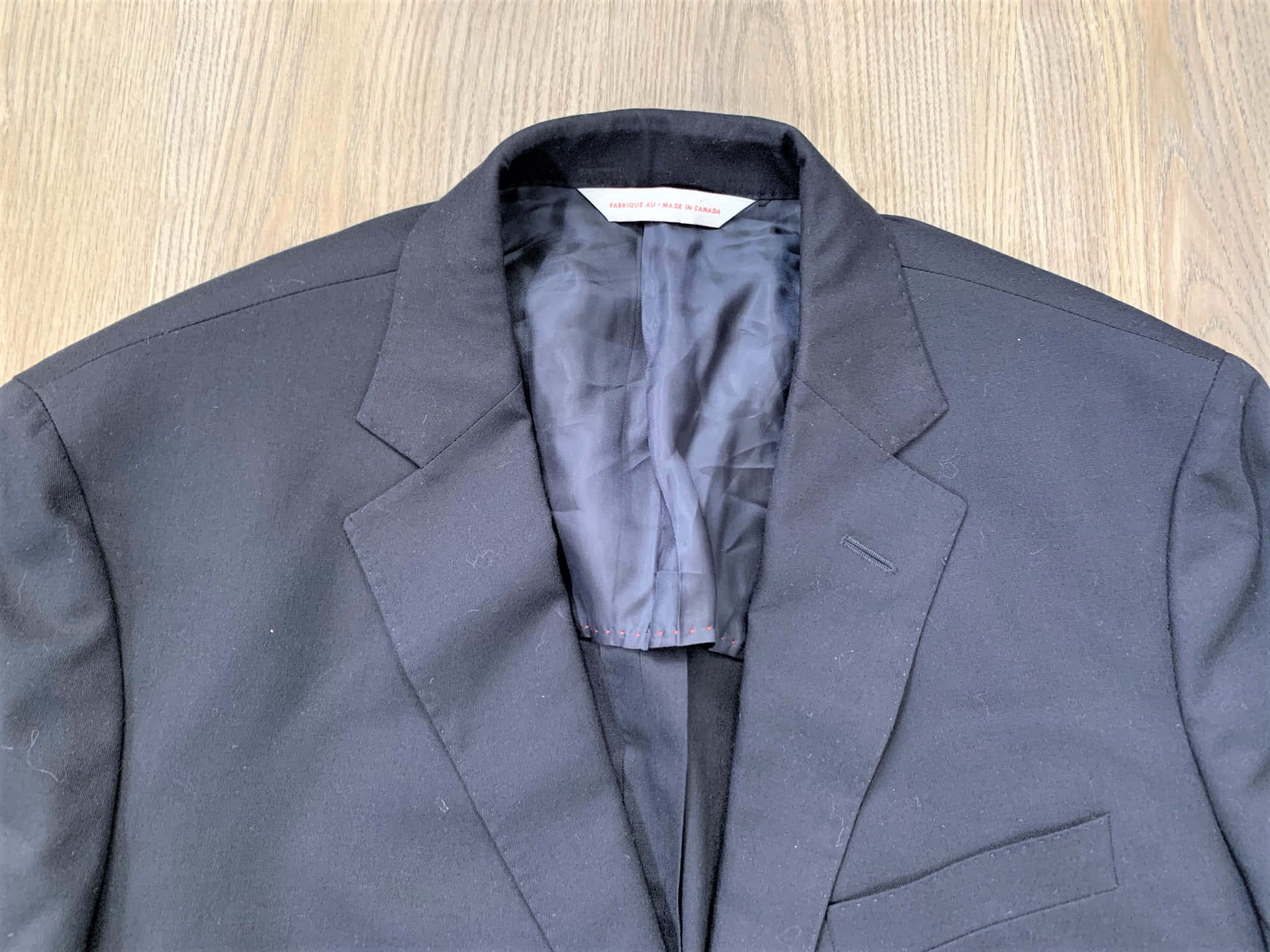 Mens Fashion 桌布 壁紙 — 淺色木質表面上平放的深灰色男士西裝外套特寫，展示領口和內裡襯裡細節。