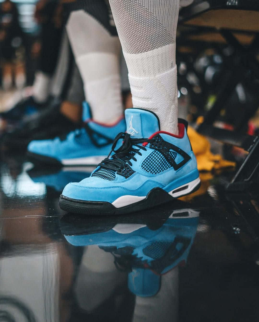 鞋子 桌布 壁紙 — 淺藍色 Jordan 4 運動鞋特寫，帶有黑色點綴和白色襪子，位於反光的籃球場地板上。
