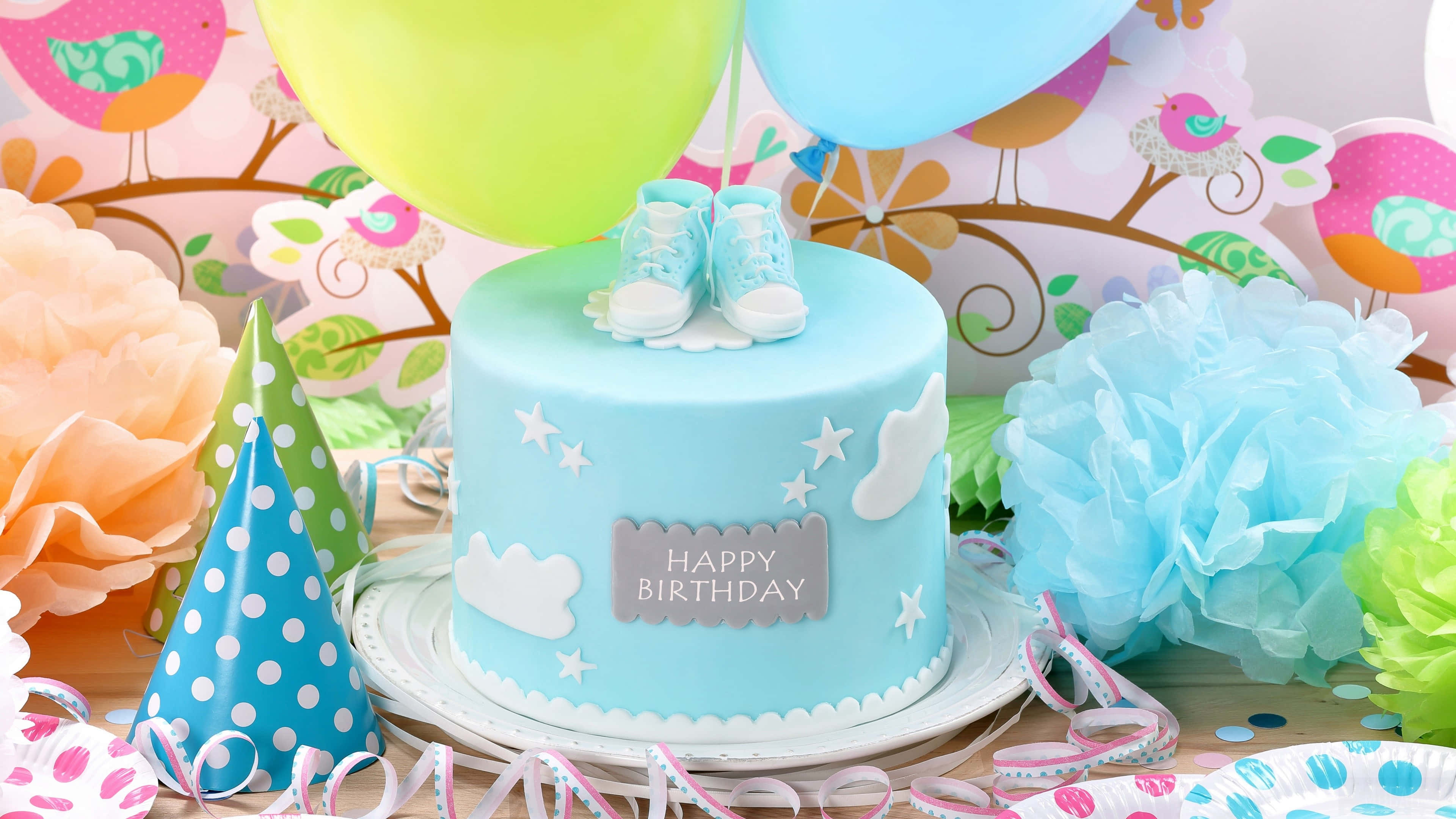 High Resolution Happy Birthday 桌布 壁紙 — 淺藍色嬰兒派對蛋糕，上面有細小的鞋子和雲朵裝飾，周圍環繞著彩色氣球和紙裝飾。