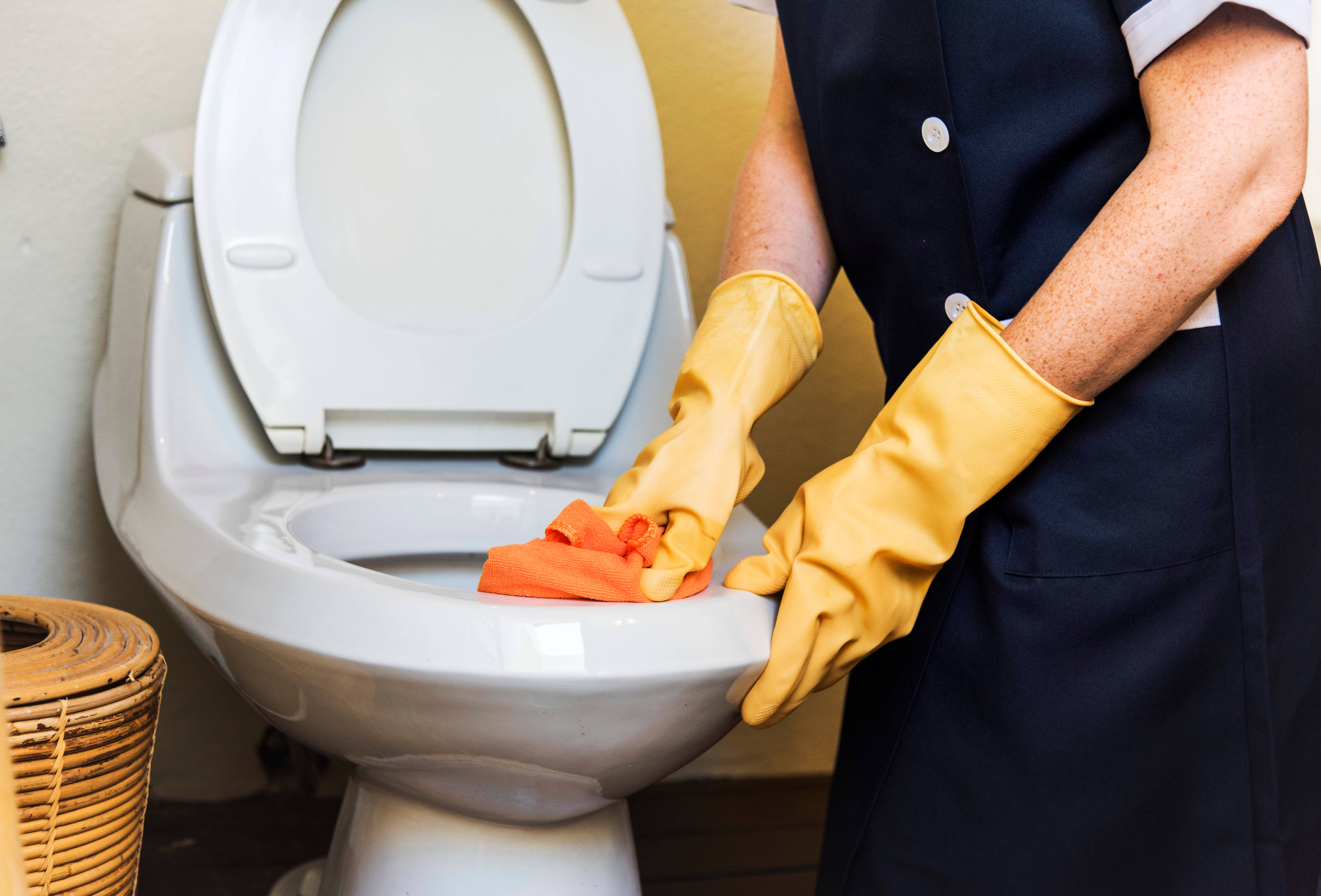 Cleaning 桌布 壁紙 — 清潔工人戴著黃色手套，在浴室用橙色布擦拭白色馬桶。