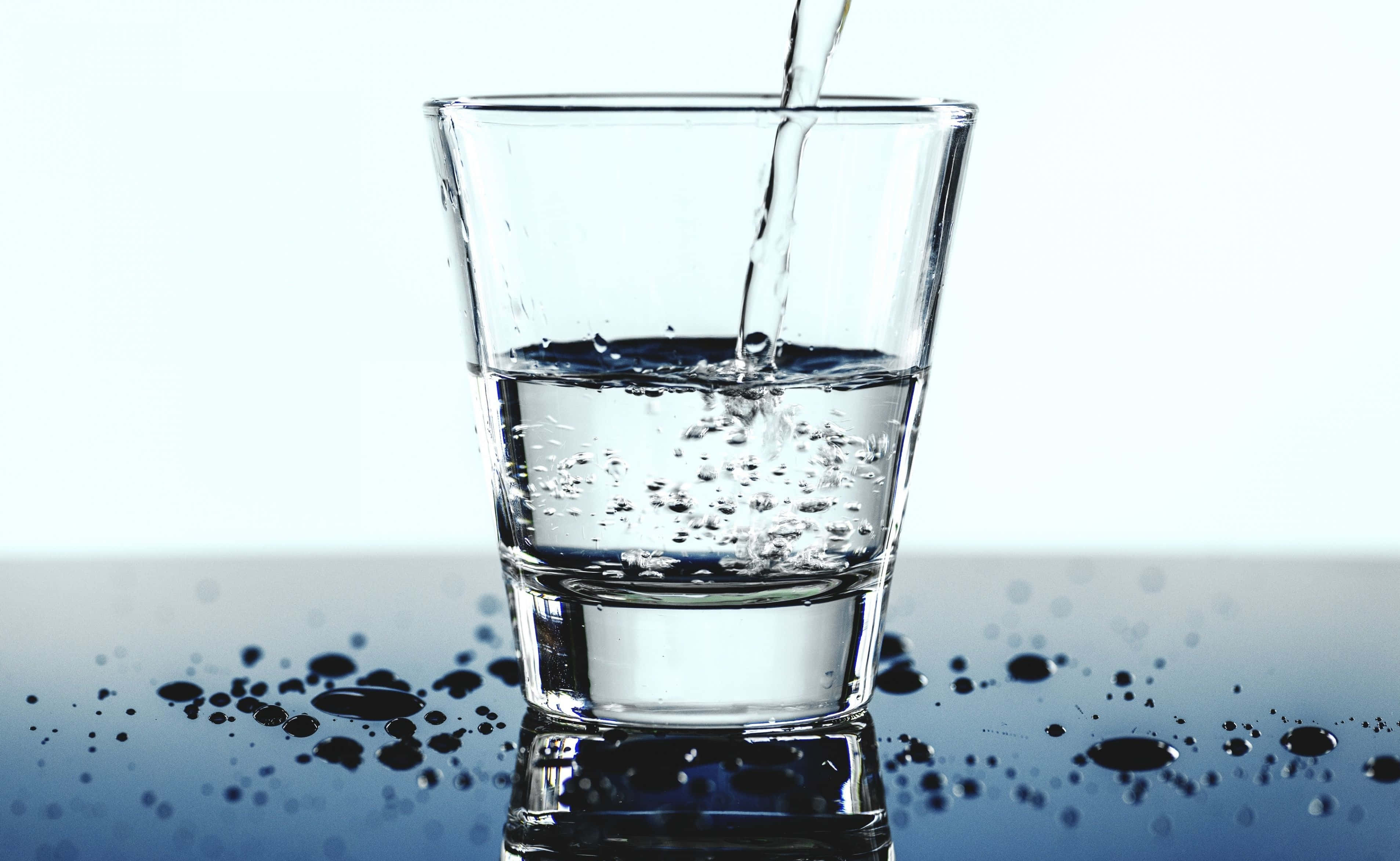 Glass Of Water 桌布 壁紙 — 清澈的水倒入玻璃杯中，在明亮的白色背景上，在反射的深色表面上產生氣泡和水滴。