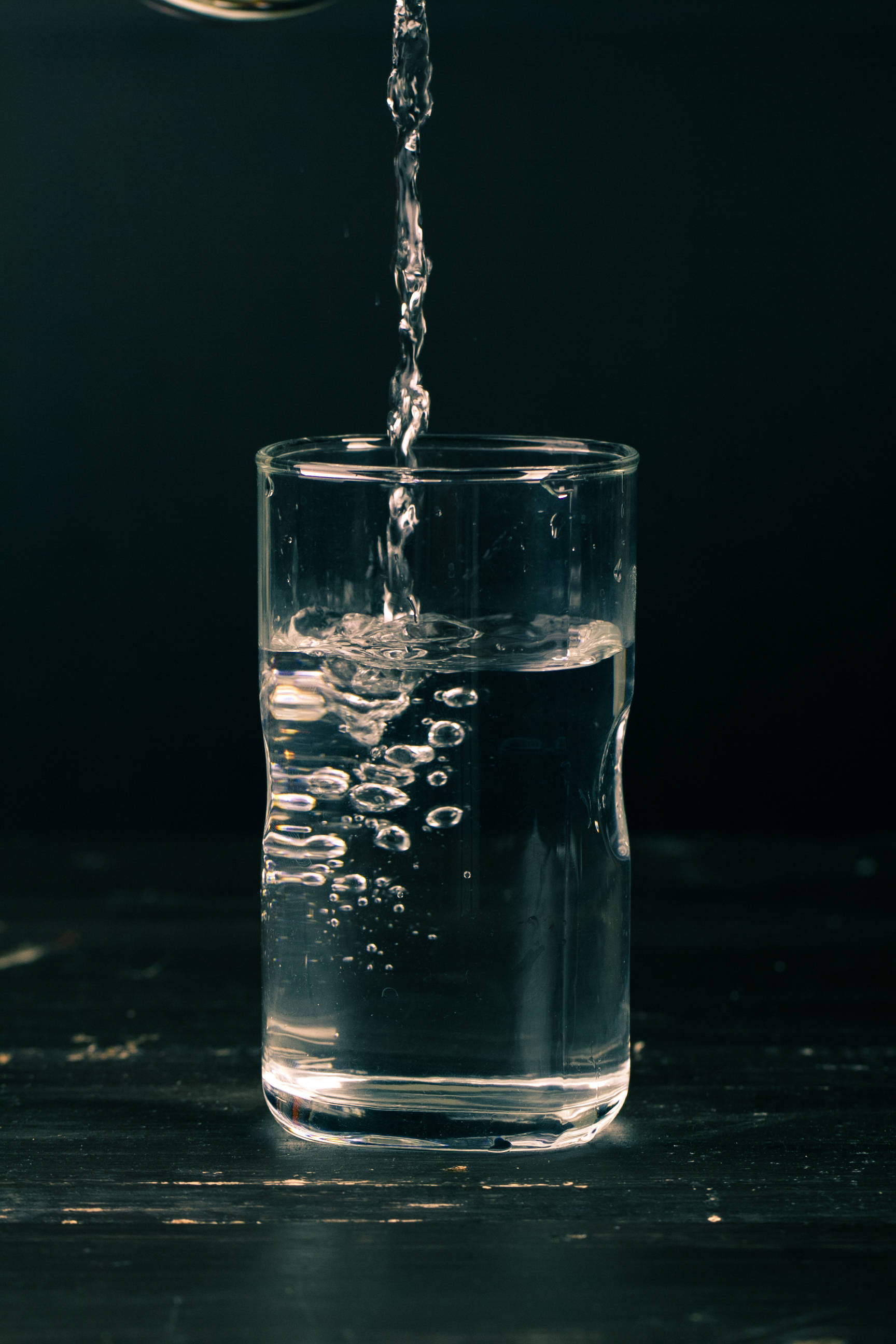 Drink 桌布 壁紙 — 清澈的水倒入玻璃杯中，在深色背景下產生氣泡。