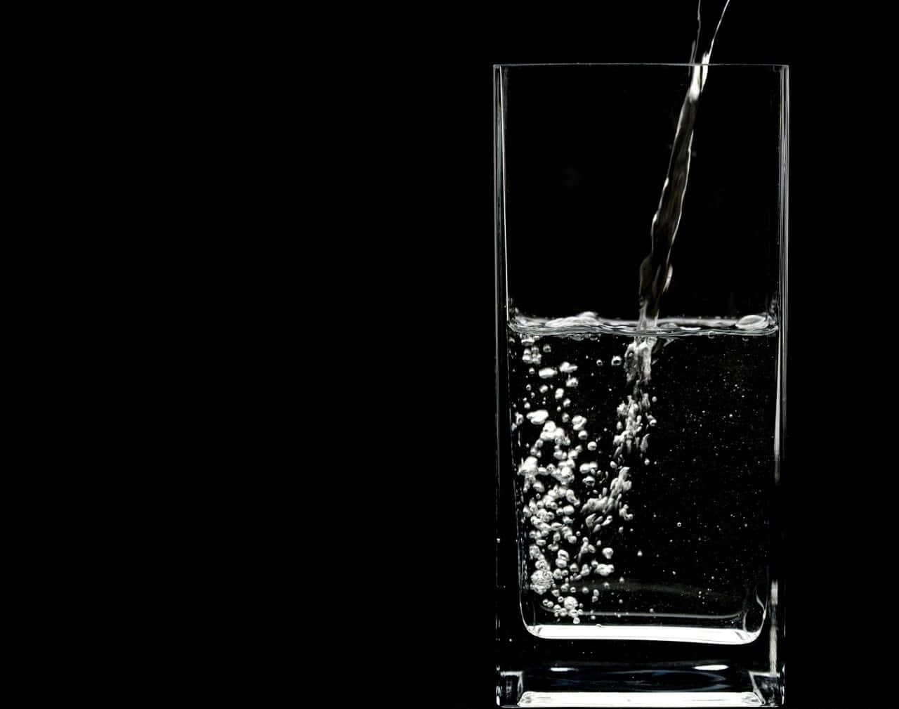 Glass Of Water 桌布 壁紙 — 清澈的水倒入玻璃杯中，背景為純黑色，產生閃閃發光的氣泡和動態運動。