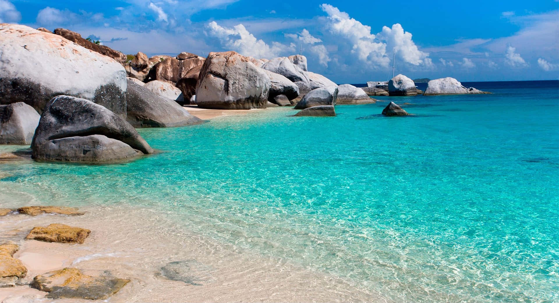 Beach Scene 桌布 壁紙 — 清澈的碧綠海水拍打著沙灘，沙灘兩旁是巨大的風化岩石，上方是明亮的藍天和蓬鬆的白雲。