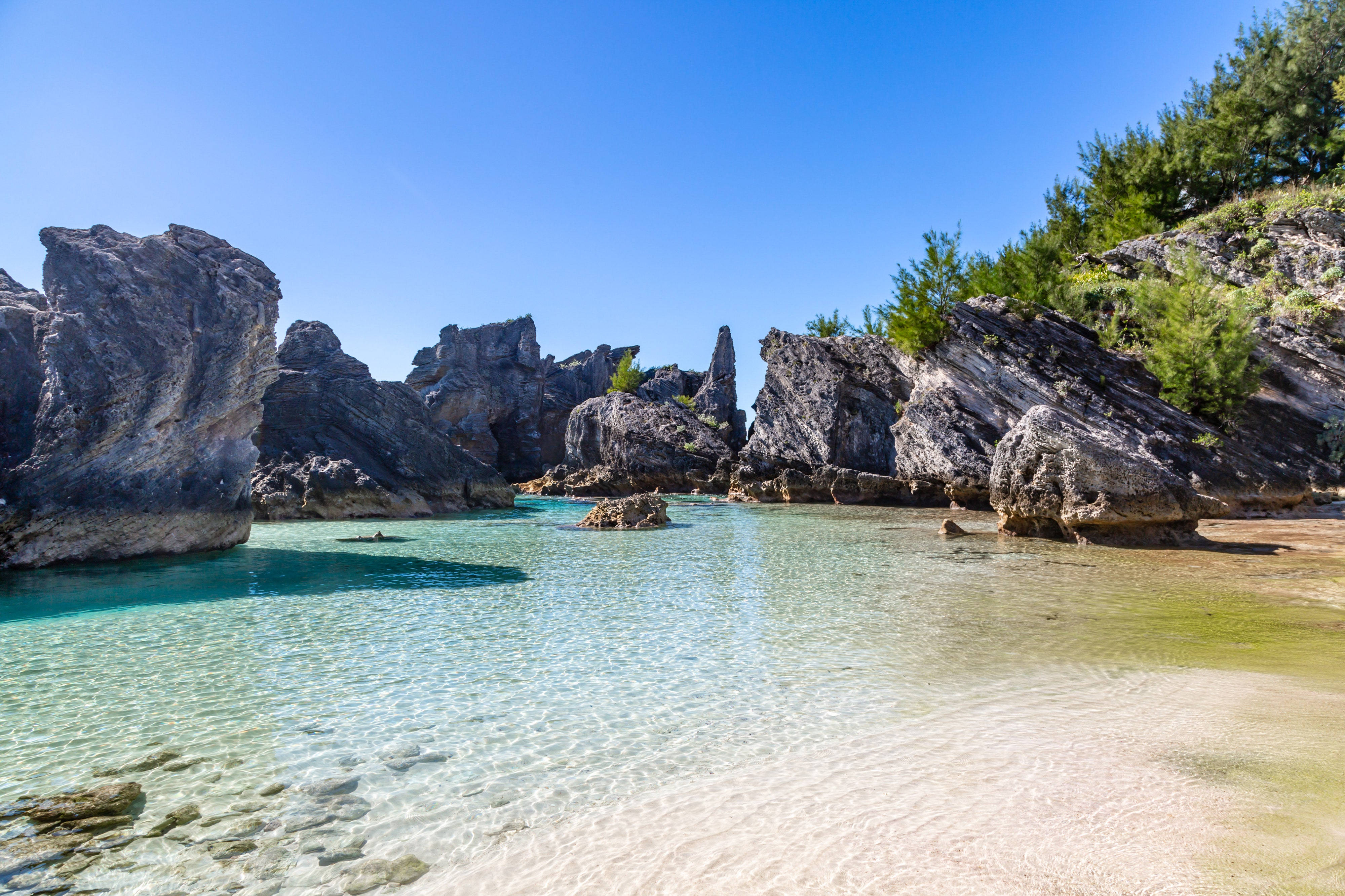 Bermuda 桌布 壁紙 — 清澈的碧綠海水拍打著白色沙灘，沙灘被戲劇性的灰色岩石形成環繞，上方是明亮的藍天。