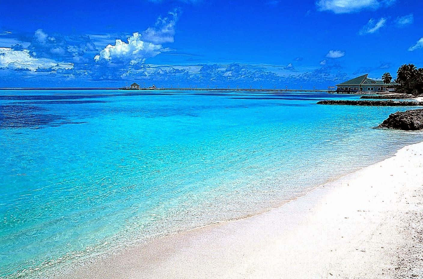 Beach Scene 桌布 壁紙 — 清澈的碧綠海水拍打著純淨的白色沙灘，上方是藍天白雲。