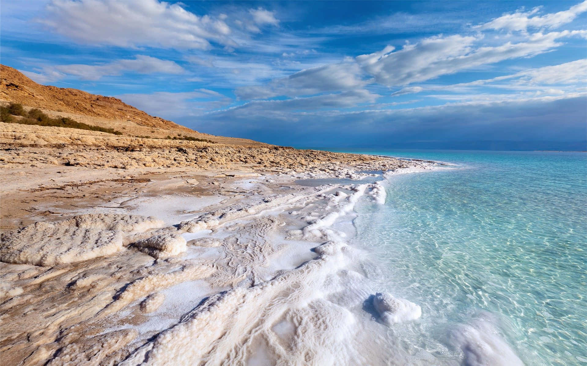 Israel 桌布 壁紙 — 清澈的碧綠海水拍打著純白色的鹽殼海岸線，在藍天白雲下閃耀。