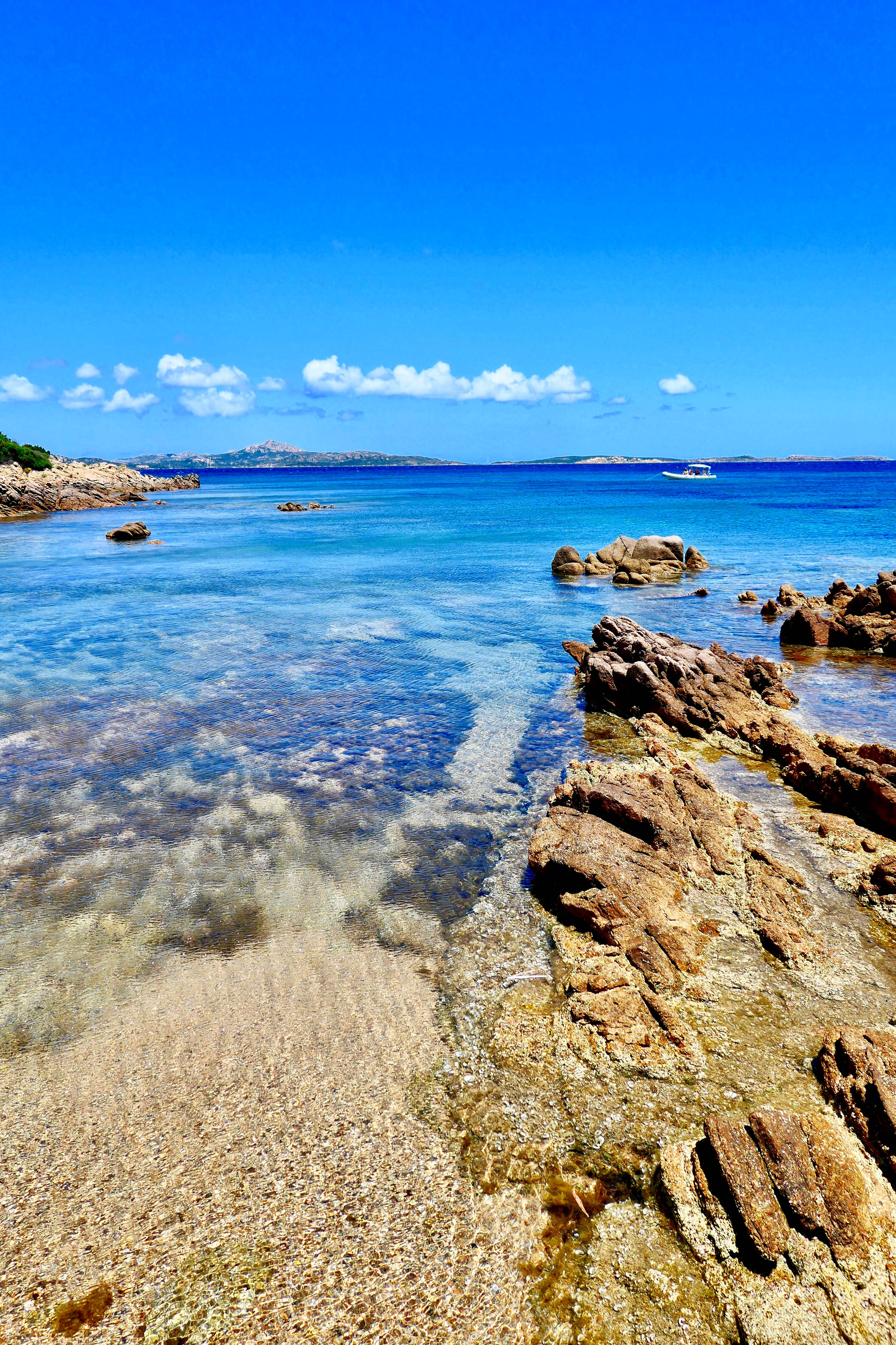 Palau 桌布 壁紙 — 清澈的碧綠海水拍打著陽光照耀的岩石海岸，上方是湛藍的天空，點綴著幾朵白雲。