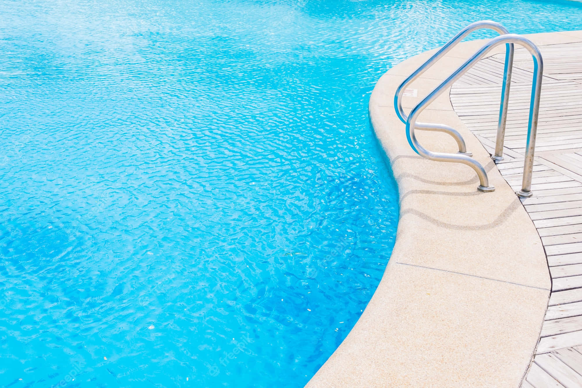 Swimming Pool 桌布 壁紙 — 清澈碧綠的泳池水在彎曲的混凝土邊緣旁泛起漣漪，旁邊有光滑的金屬梯子和木質甲板。