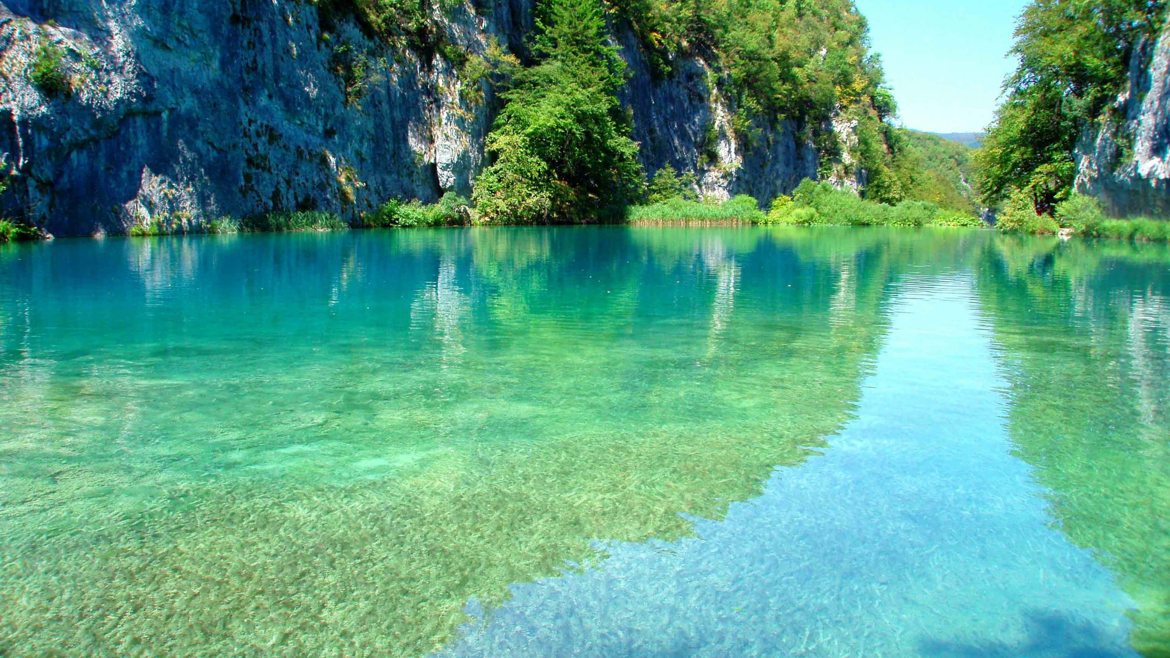 Lake 桌布 壁紙 — 清澈碧綠的海水倒映著高聳的綠色懸崖，天空湛藍明亮。
