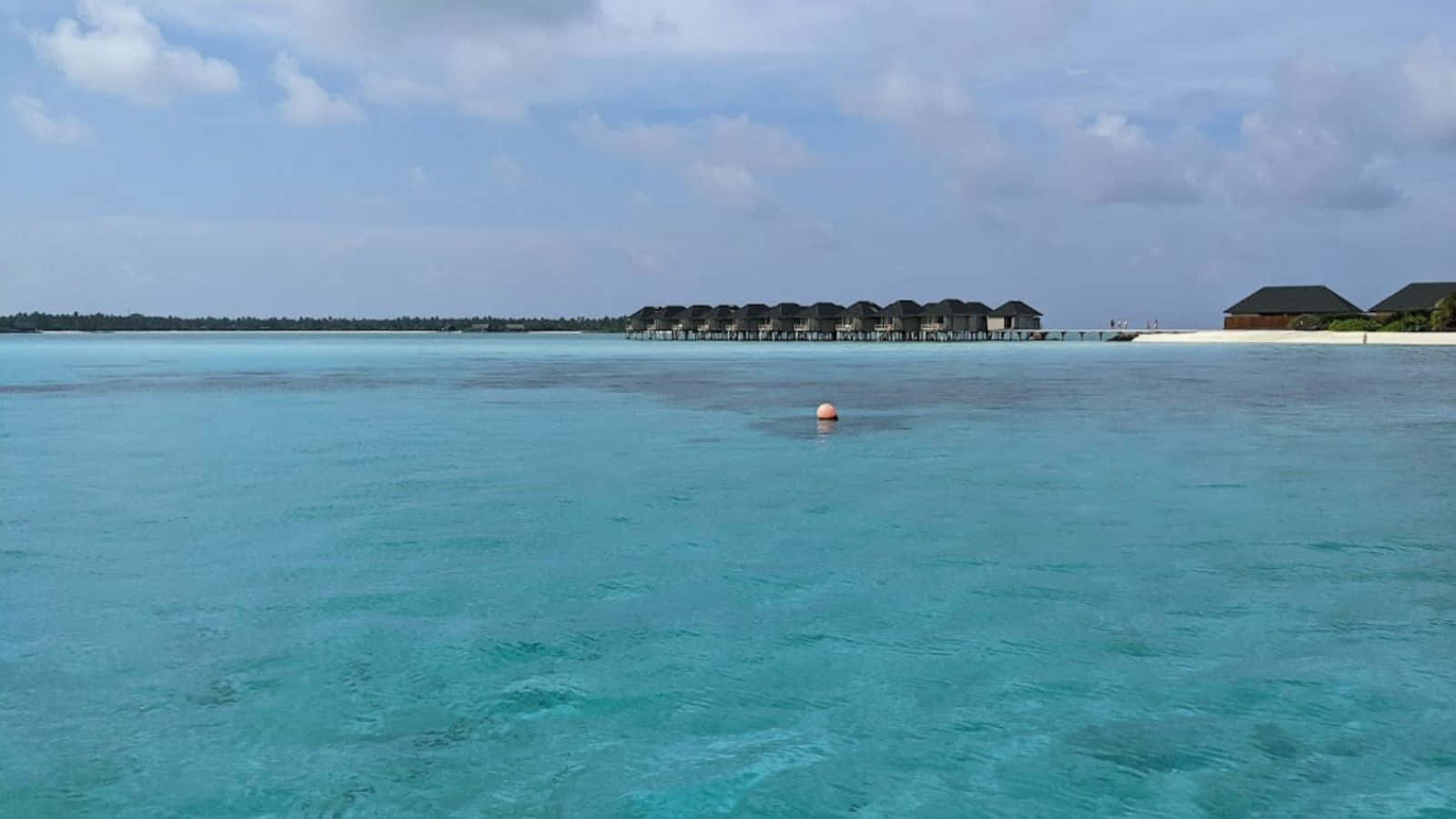 馬爾地夫 桌布 壁紙 — 清澈碧綠的海水延伸到水上平房，上方是部分多雲的藍天。