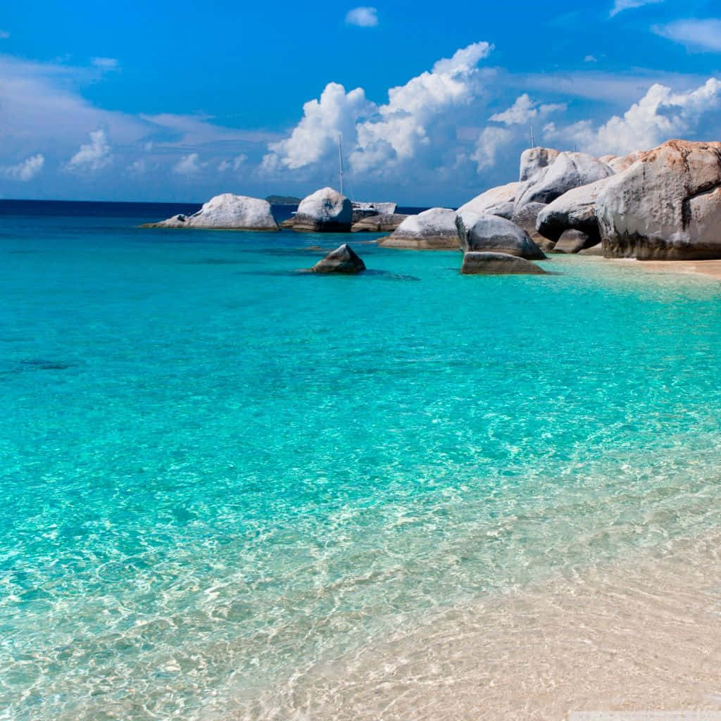 Beach Aesthetic 桌布 壁紙 — 清澈碧綠的海水拍打著沙灘，沙灘上有巨大的白色岩石和帆船，天空湛藍，白雲朵朵。