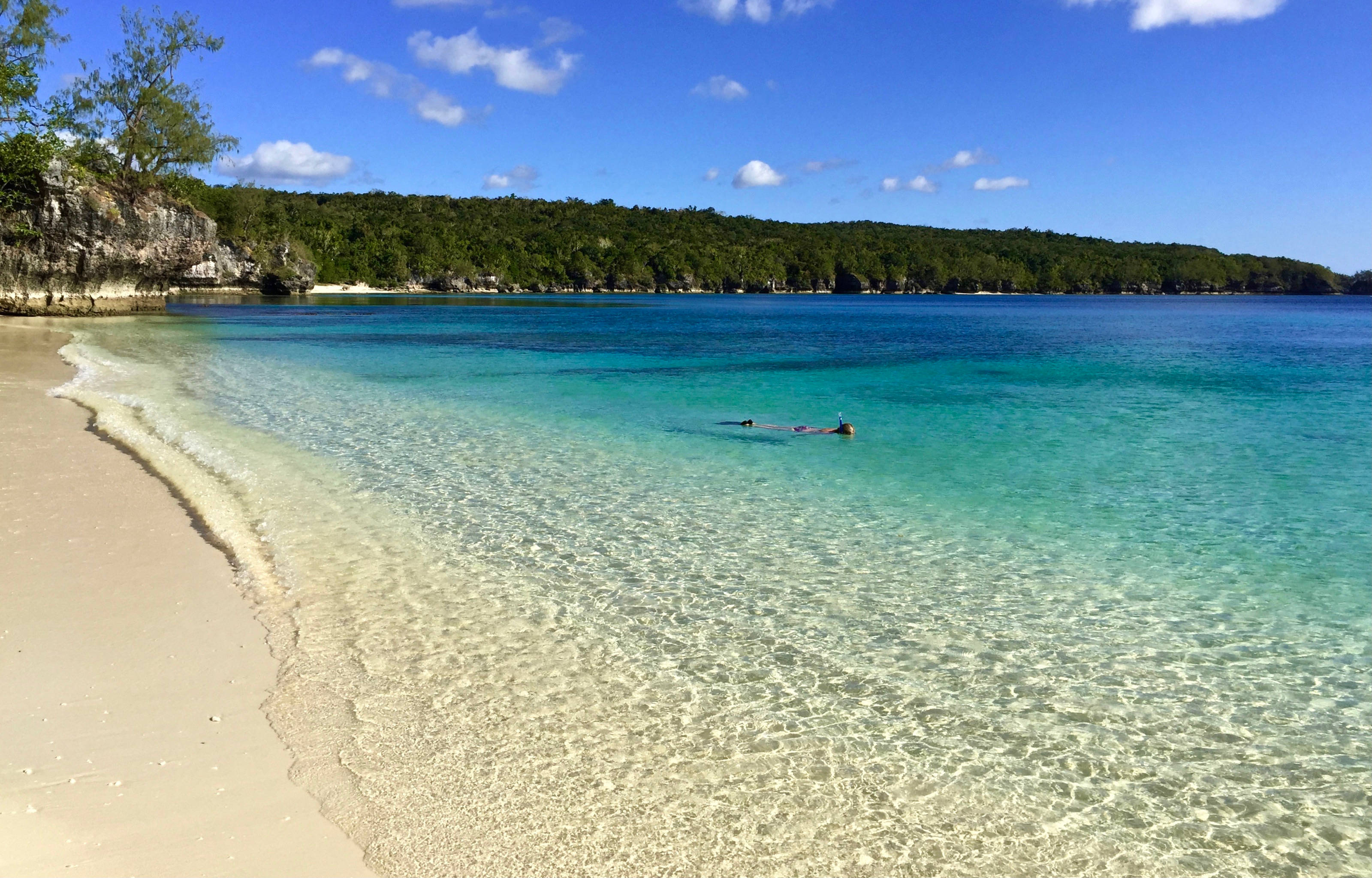 Vanuatu 桌布 壁紙 — 清澈碧綠的海水輕拍著粉白色的沙灘，兩位游泳者在明亮的藍天下享受平靜的海面。