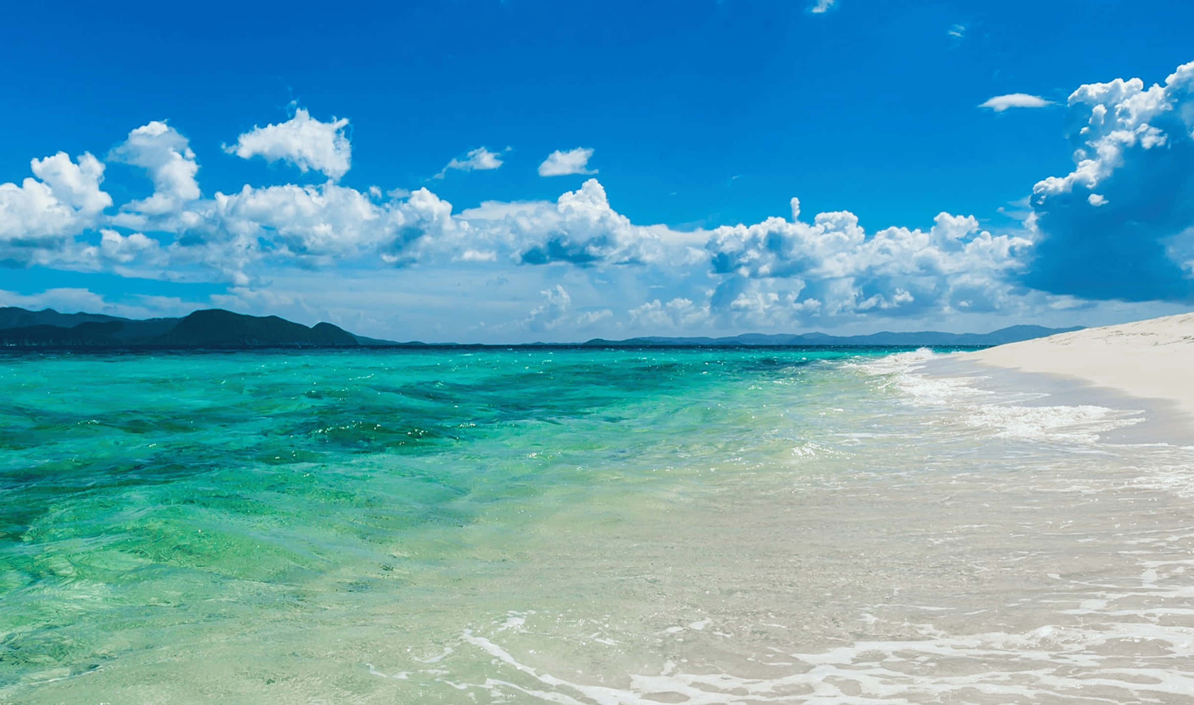 2440x1440 Monitor 桌布 壁紙 — 清澈碧綠的海水輕拍著純白沙灘，上方是藍天白雲。
