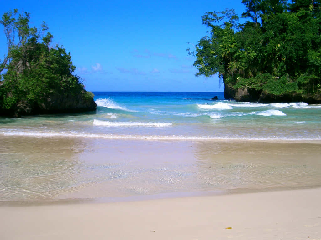 Jamaican Island 桌布 壁紙 — 清澈碧綠的海水輕輕拍打著原始沙灘，沙灘兩旁是鬱鬱蔥蔥的綠色懸崖，上方是明亮的藍天。