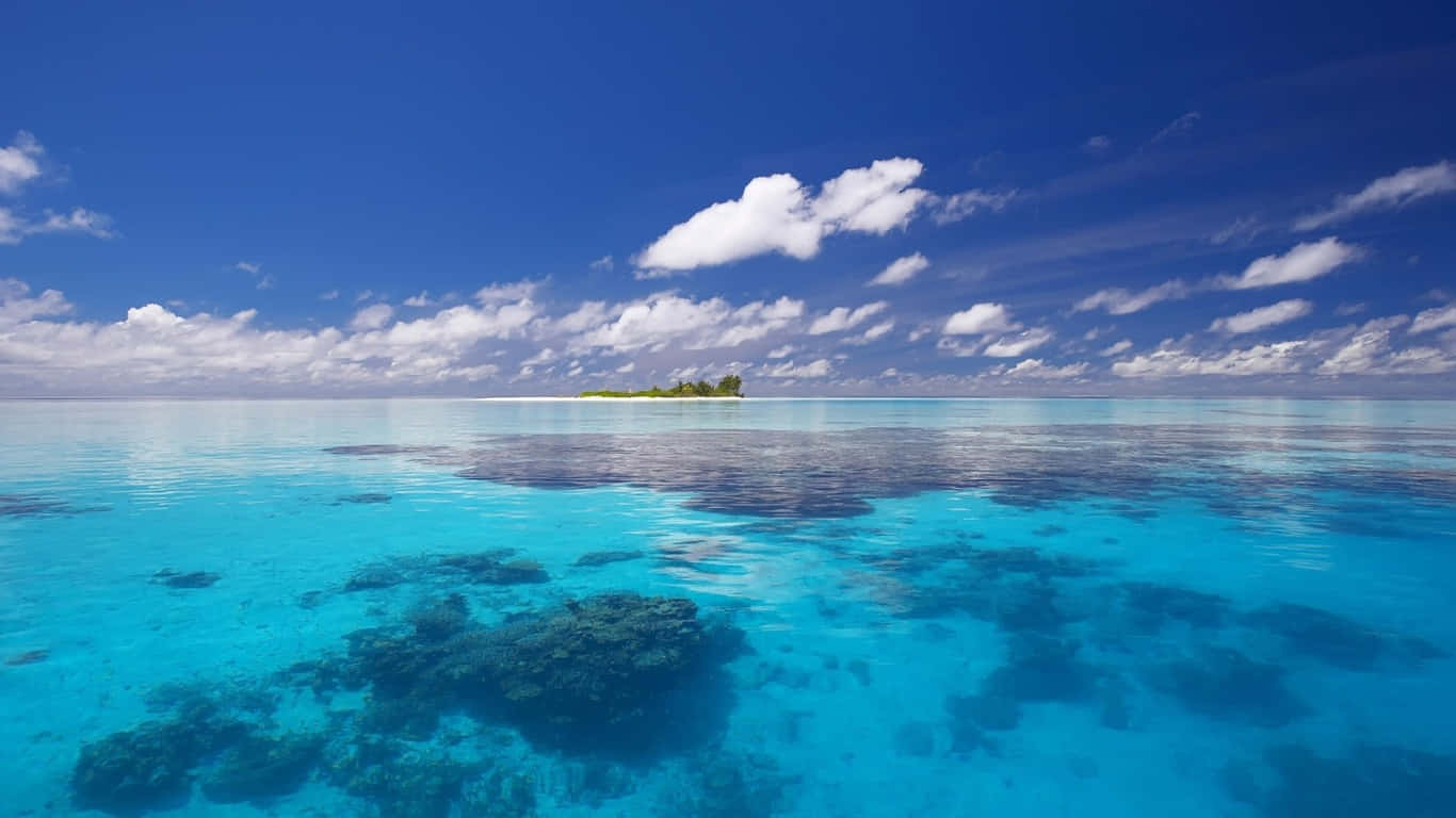 島嶼 桌布 壁紙 — 清澈碧綠的海水顯露出珊瑚礁，上方是點綴著蓬鬆白雲的湛藍天空。