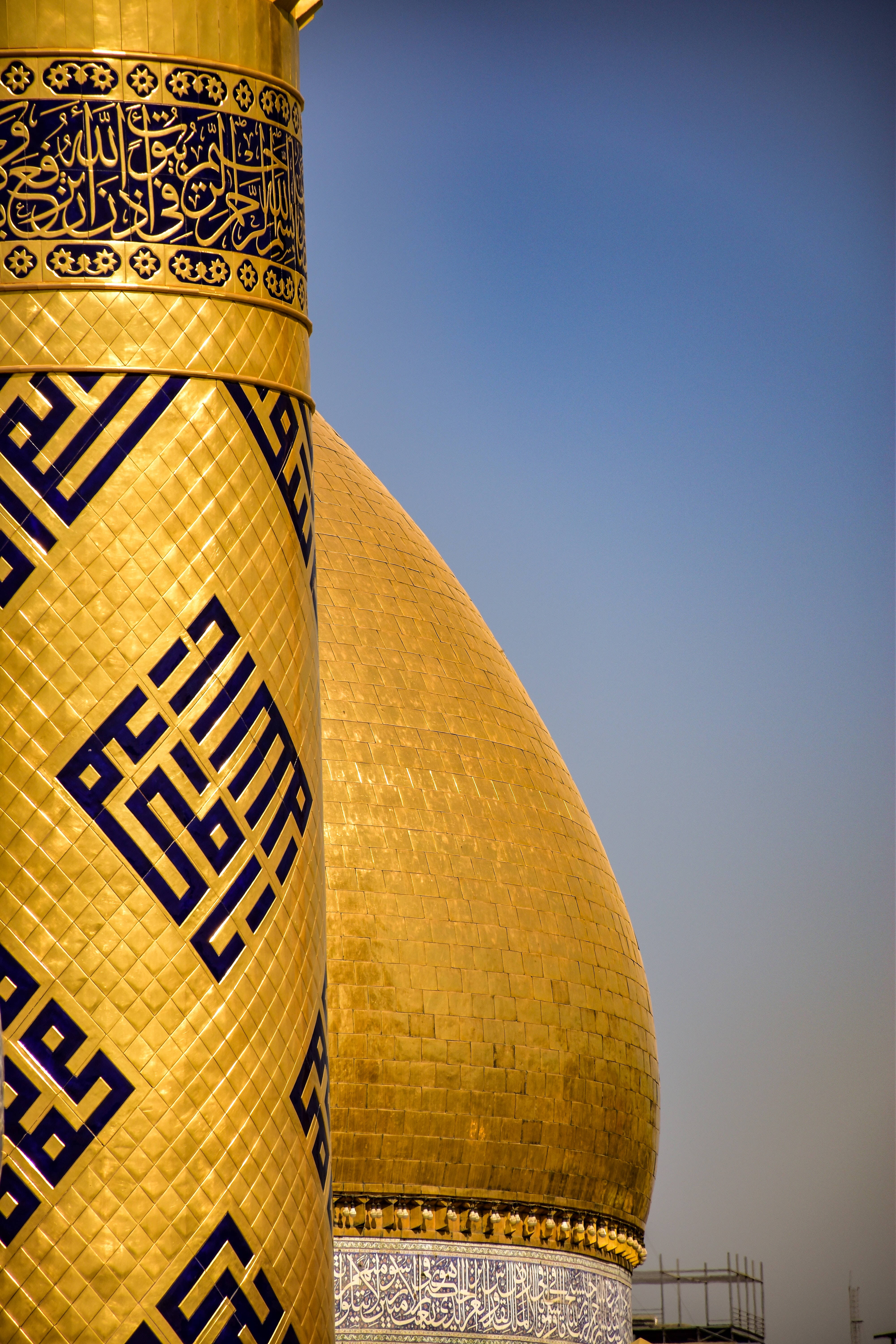 Iraq 桌布 壁紙 — 清真寺的金色圓頂和宣禮塔在清澈的藍天下閃耀，帶有精緻的藍色瓷磚工藝和書法。