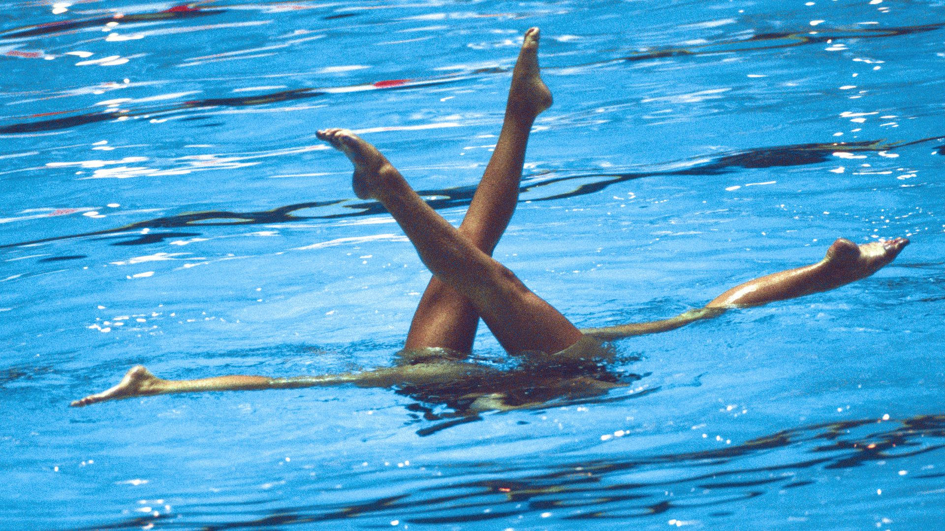 Swimming 桌布 壁紙 — 游泳者的雙腿在陽光照射下波光粼粼的藍色泳池水面上形成動態的X形。