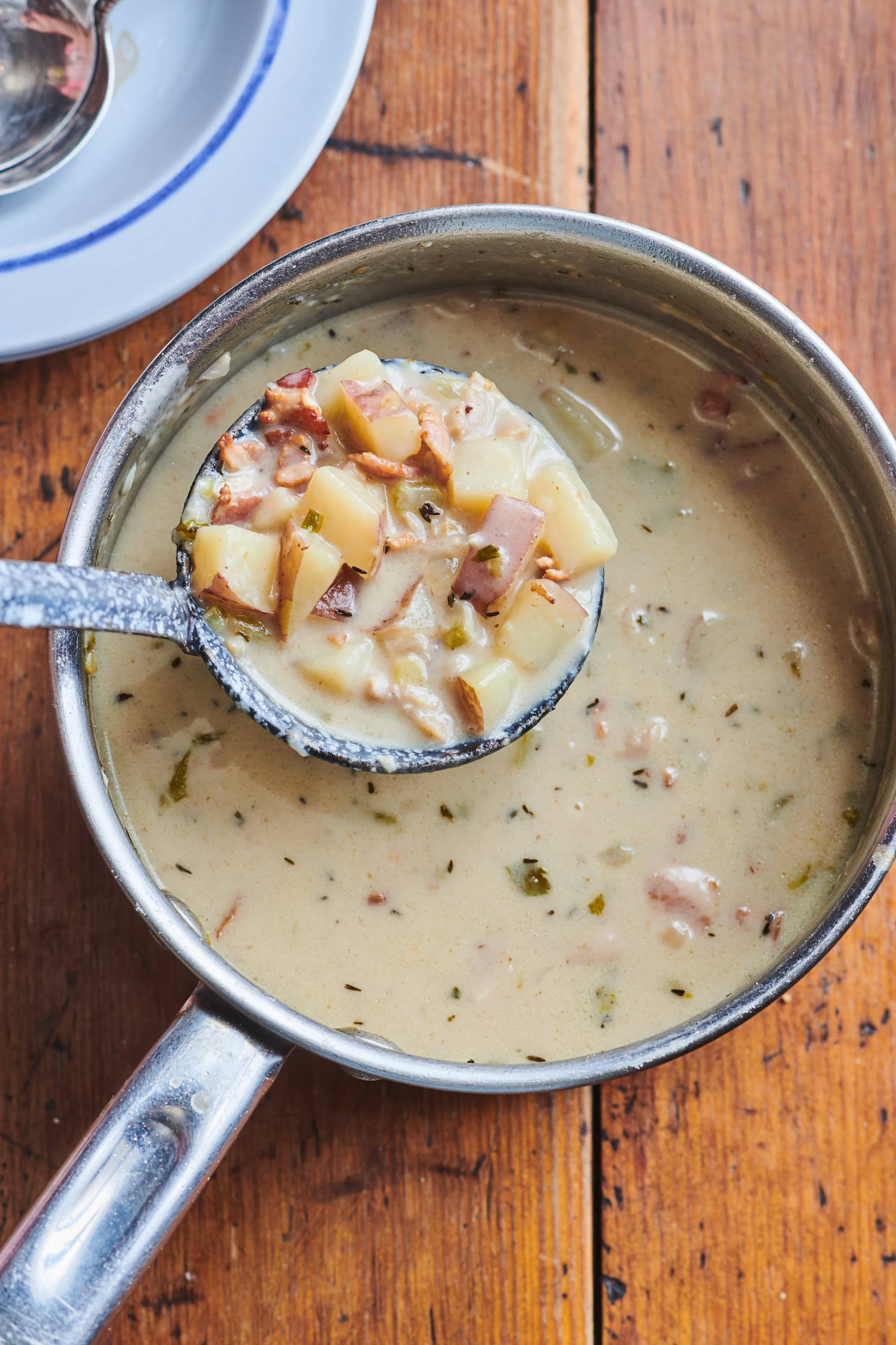 Chowder 桌布 壁紙 — 湯勺從一個鄉村木桌上的不鏽鋼鍋中舀起帶有馬鈴薯和培根塊的奶油蛤蜊湯。