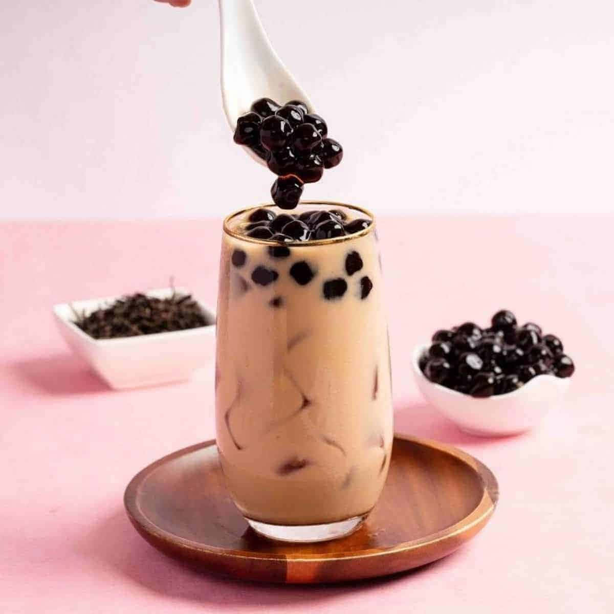 Boba Tea 桌布 壁紙 — 湯匙從木杯墊上的玻璃杯中舀起奶油冰奶茶中的光滑黑色珍珠。