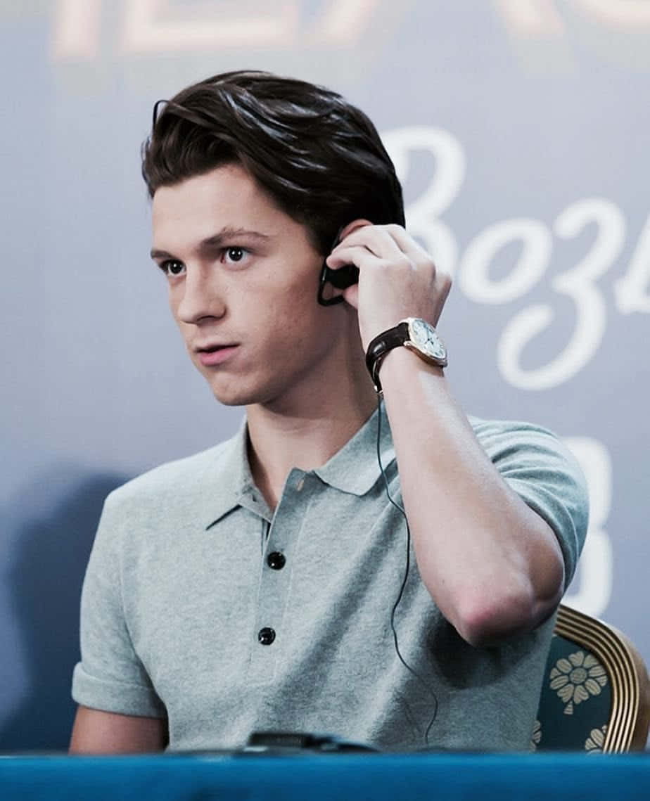Tom Holland Aesthetic 桌布 壁紙 — 湯姆·霍蘭德戴著淺灰色Polo衫和手錶，調整黑色耳機。