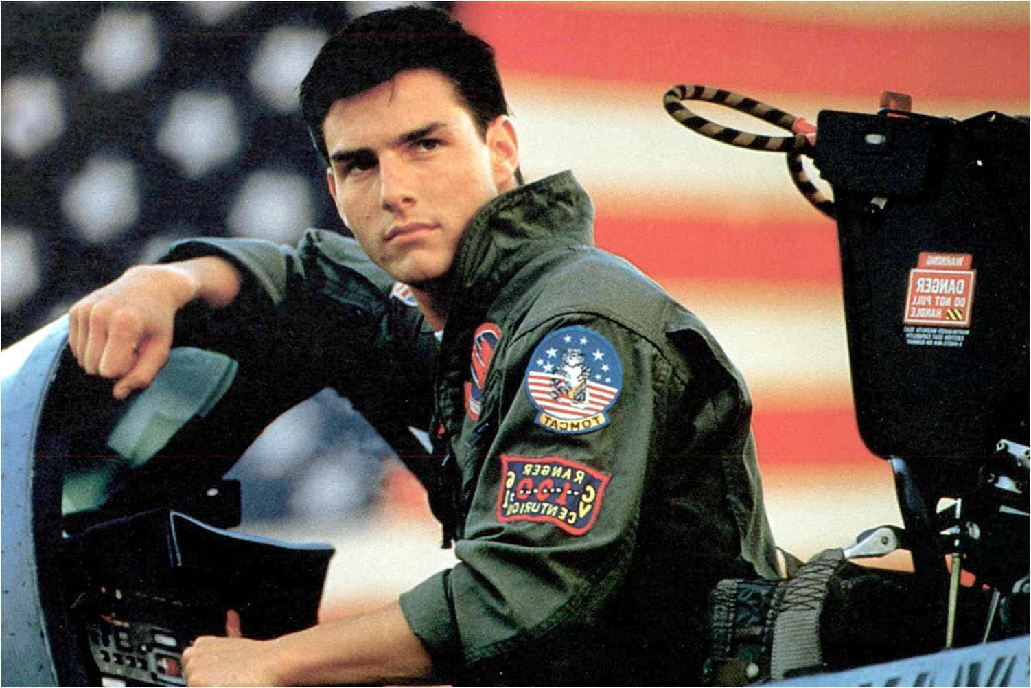 Top Gun 桌布 壁紙 — 湯姆克魯斯以戰鬥機飛行員身份自信地靠在駕駛艙內，背景是模糊的美國國旗。