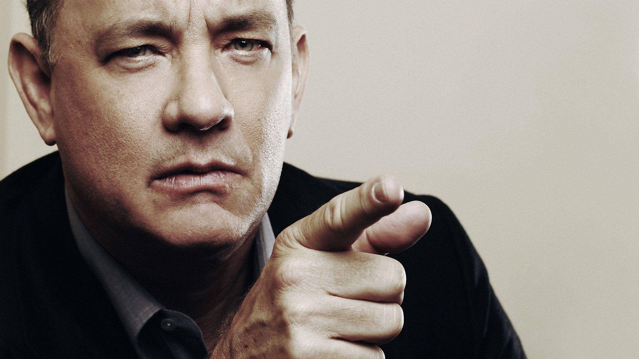 Tom Hanks 桌布 壁紙 — 湯姆漢克斯在強烈燈光的特寫肖像中，專注地盯著觀眾，同時用手指直接指向觀眾。