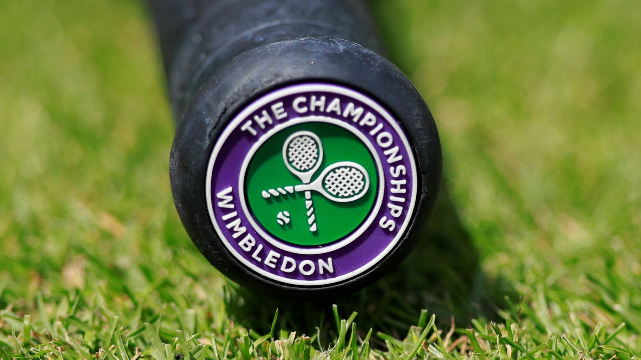 Wimbledon 桌布 壁紙 — 溫布頓網球拍手柄特寫，帶有官方標誌，置於充滿活力的綠色草地上。